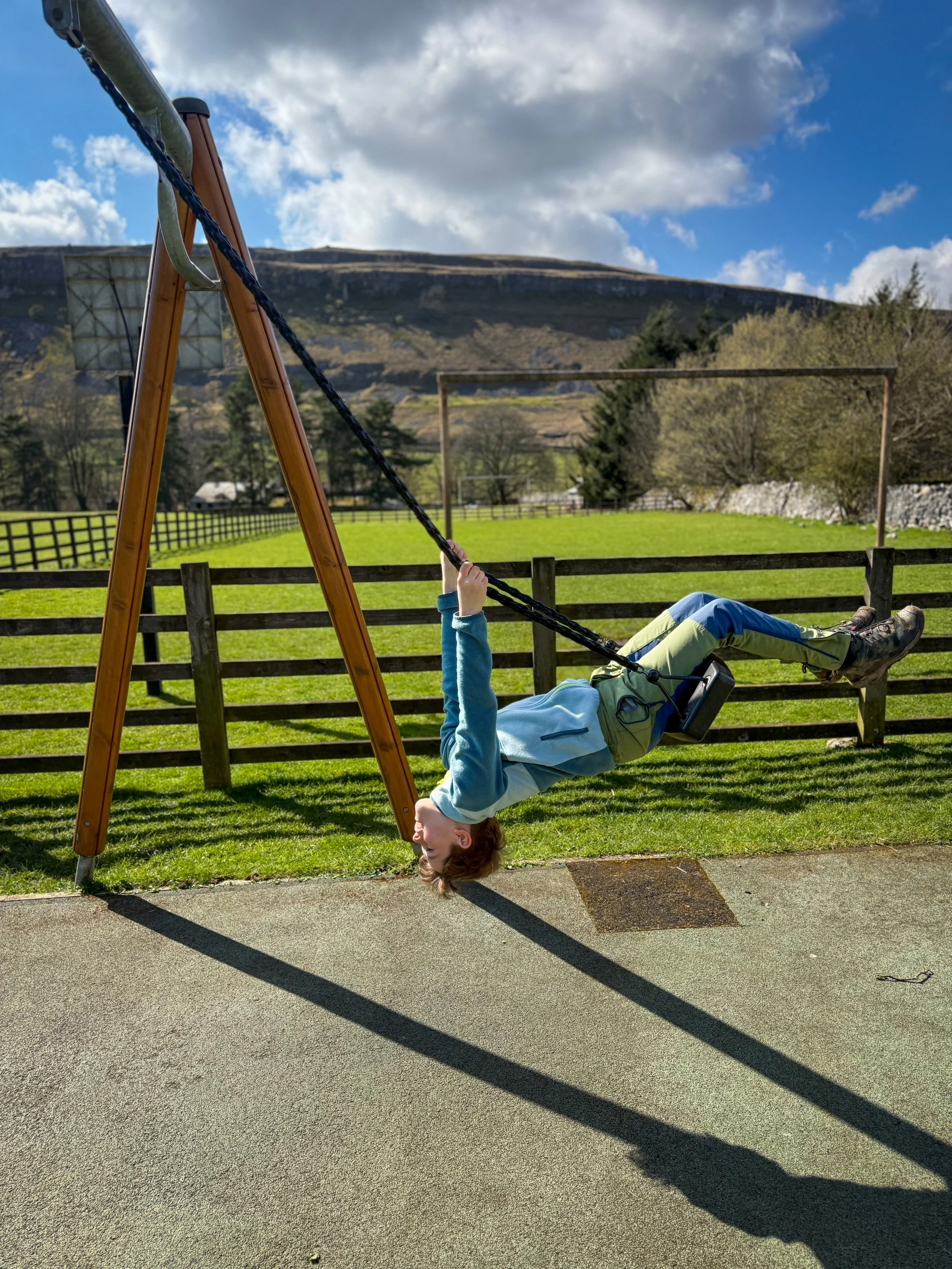 Child leaning back on a swing with a large craggy fell behind