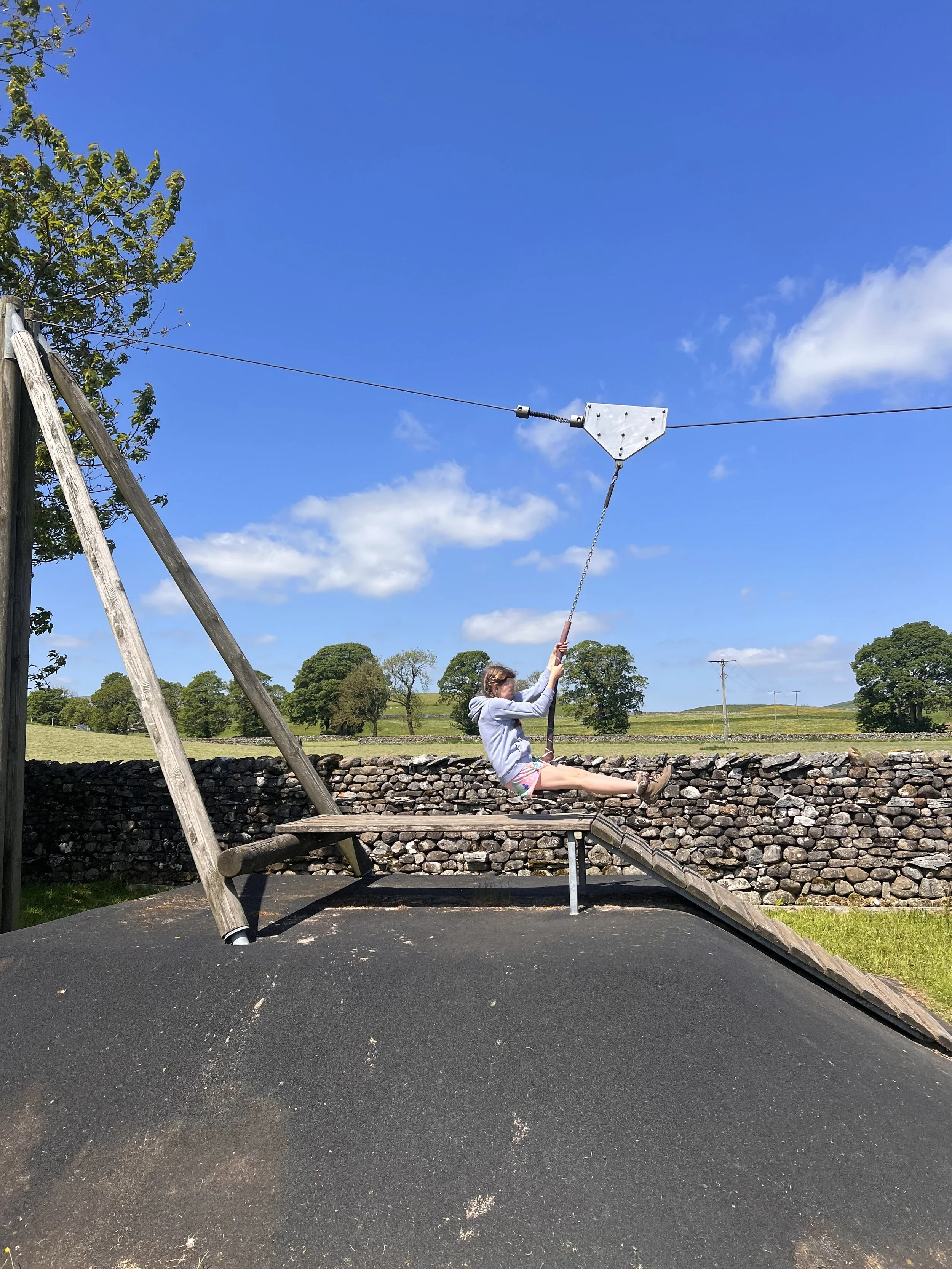 Child in motion on a zipline with blue skies above and dry stone wall behind