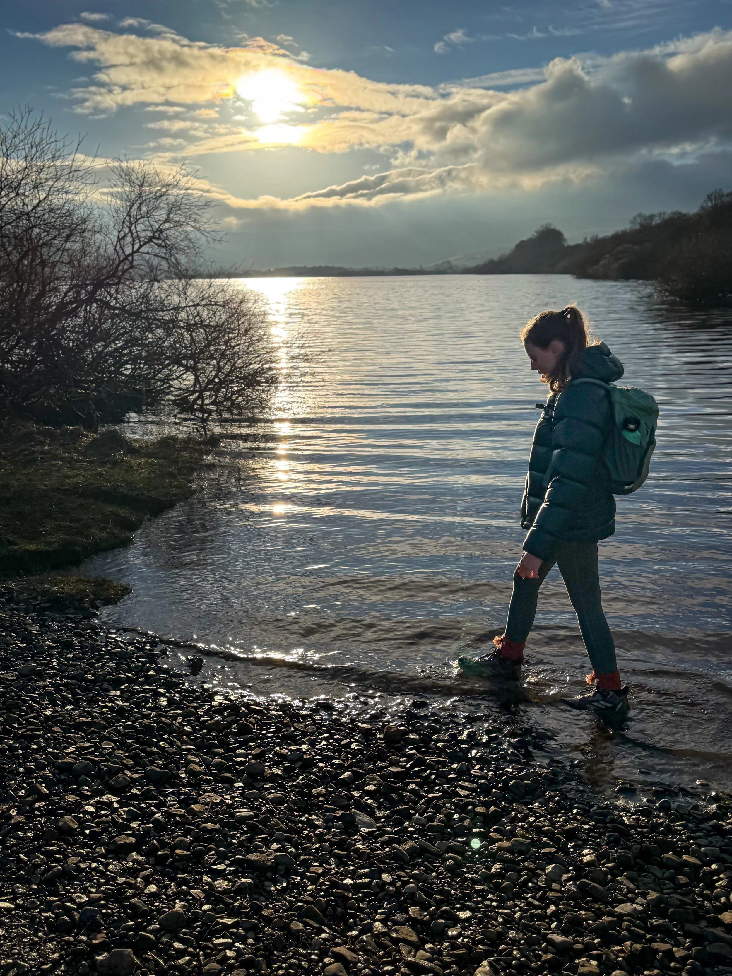 Child walking in the water of a lake with low sun behind shot