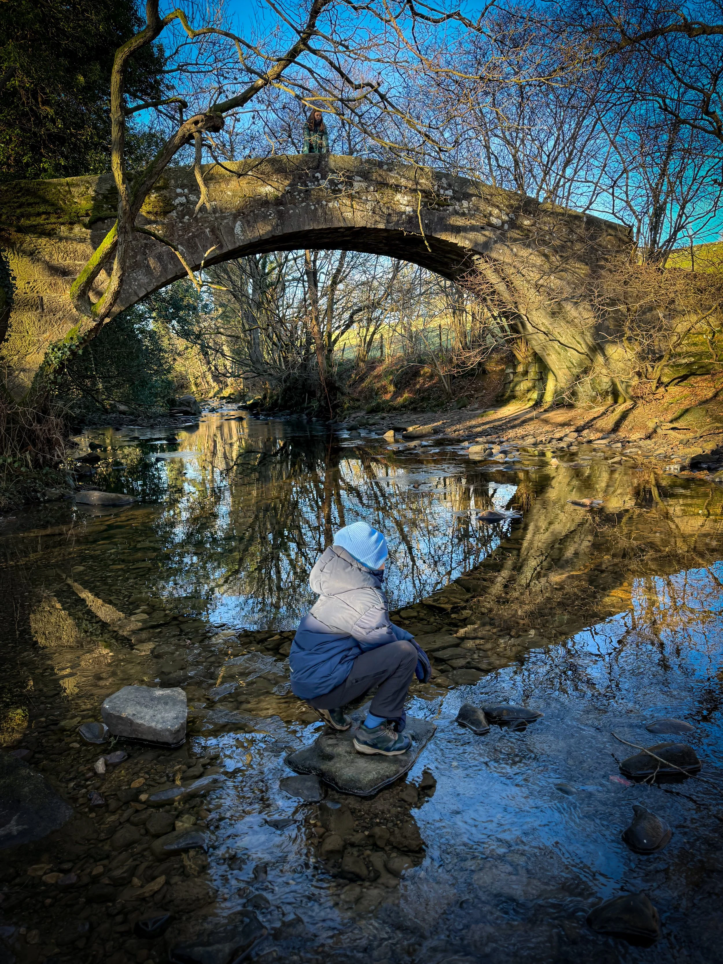 Child sat on rock in river next to Dob Park bridge