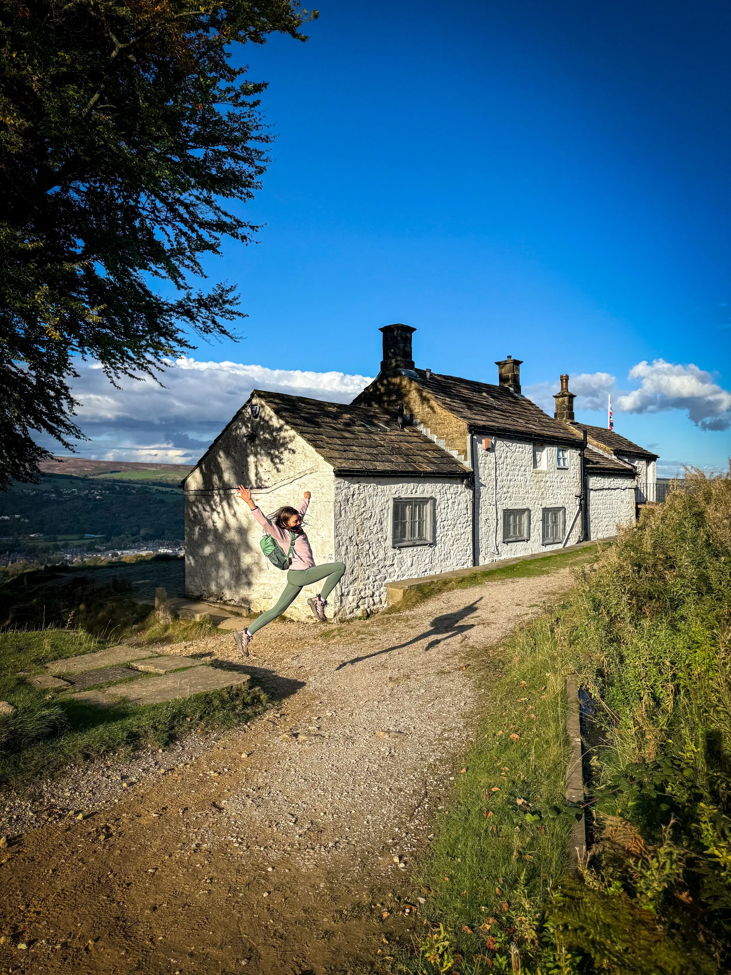 The white building of white wells spa on ilkley moor with a child in front under blue skies in late summer with views beyond to moors