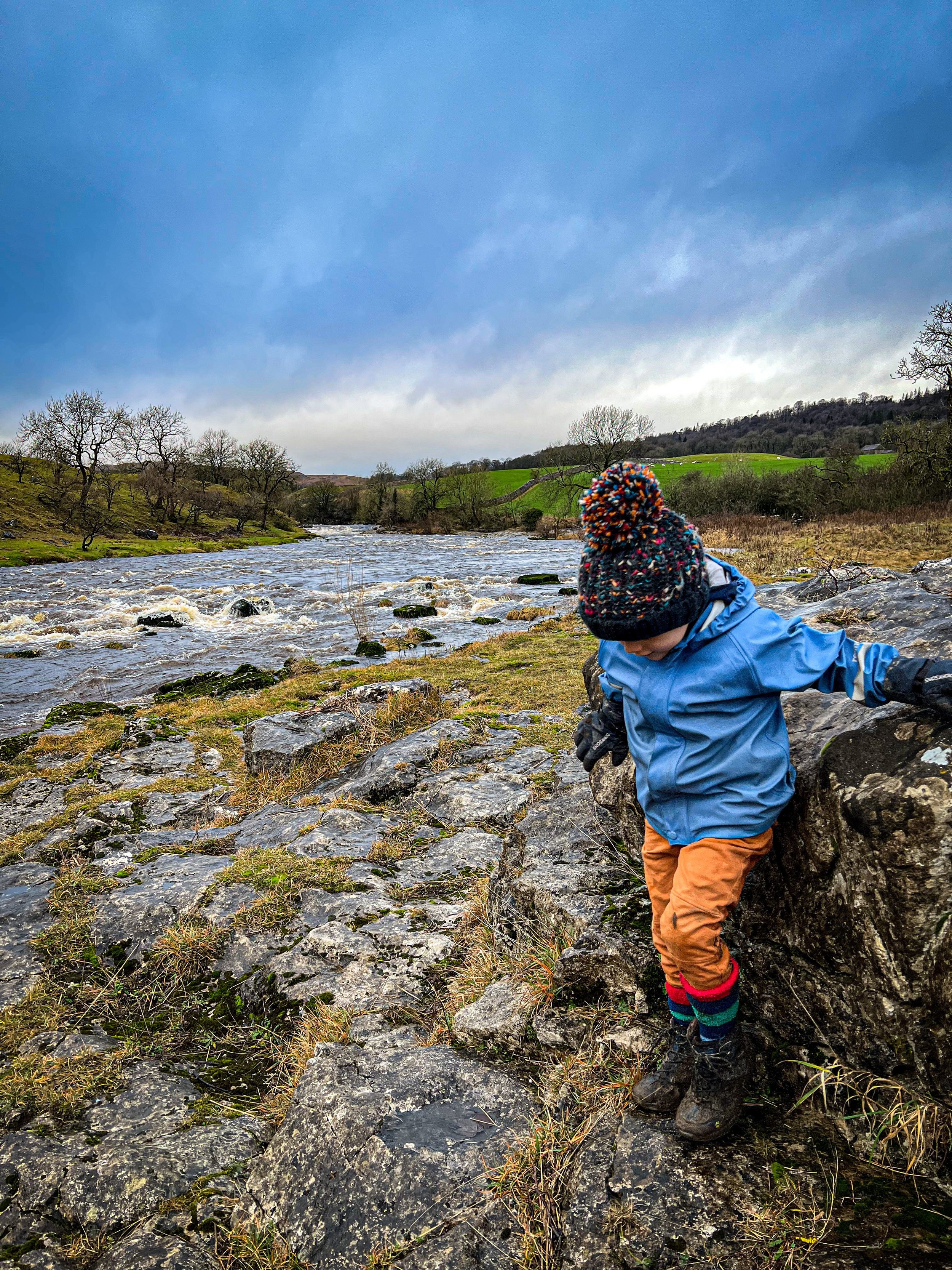 Child in wooly hat in winter next to a raging river in spate