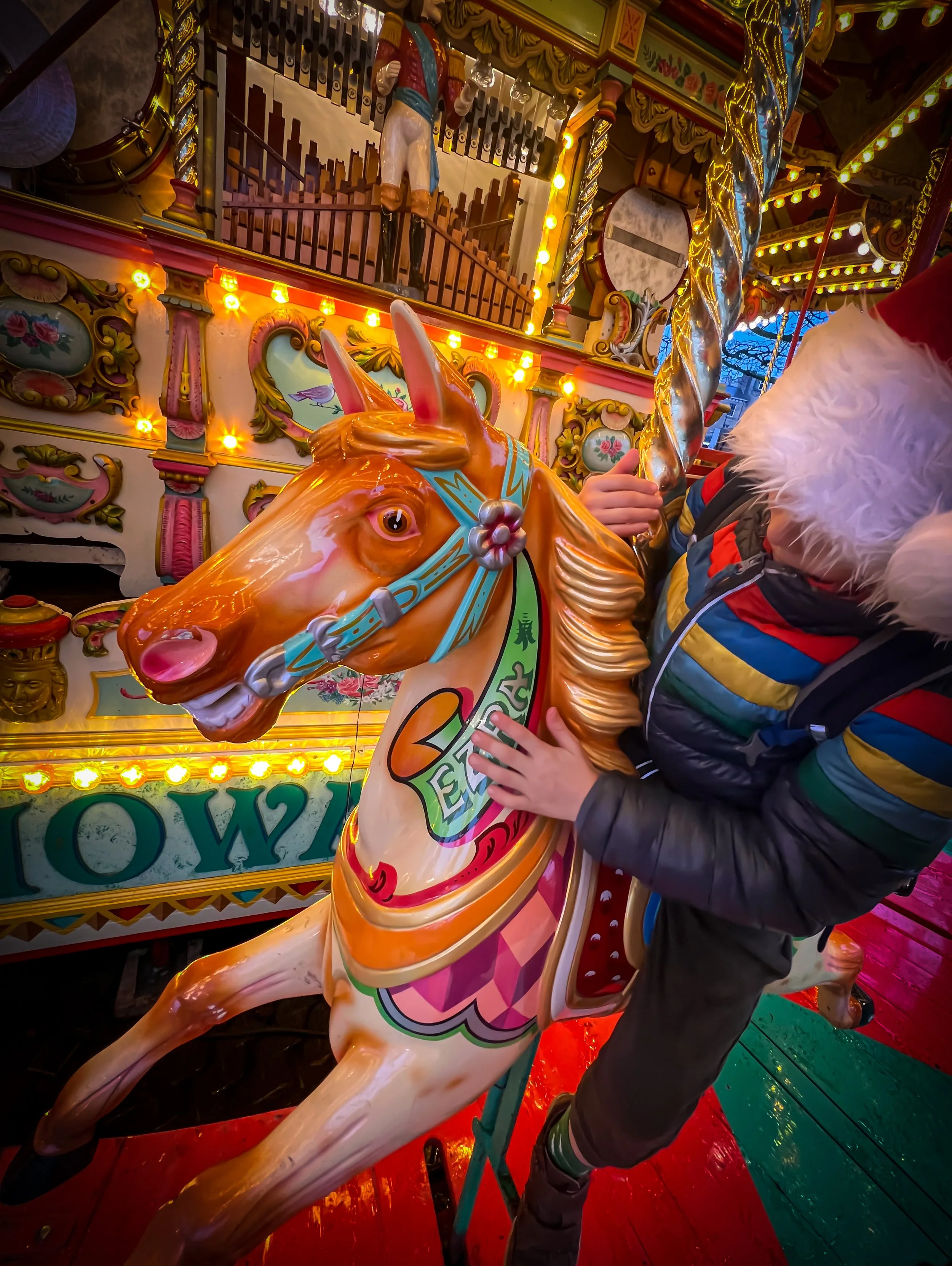 Child wearing a santa's hat sat on a carousel horse with a pipe organ behind