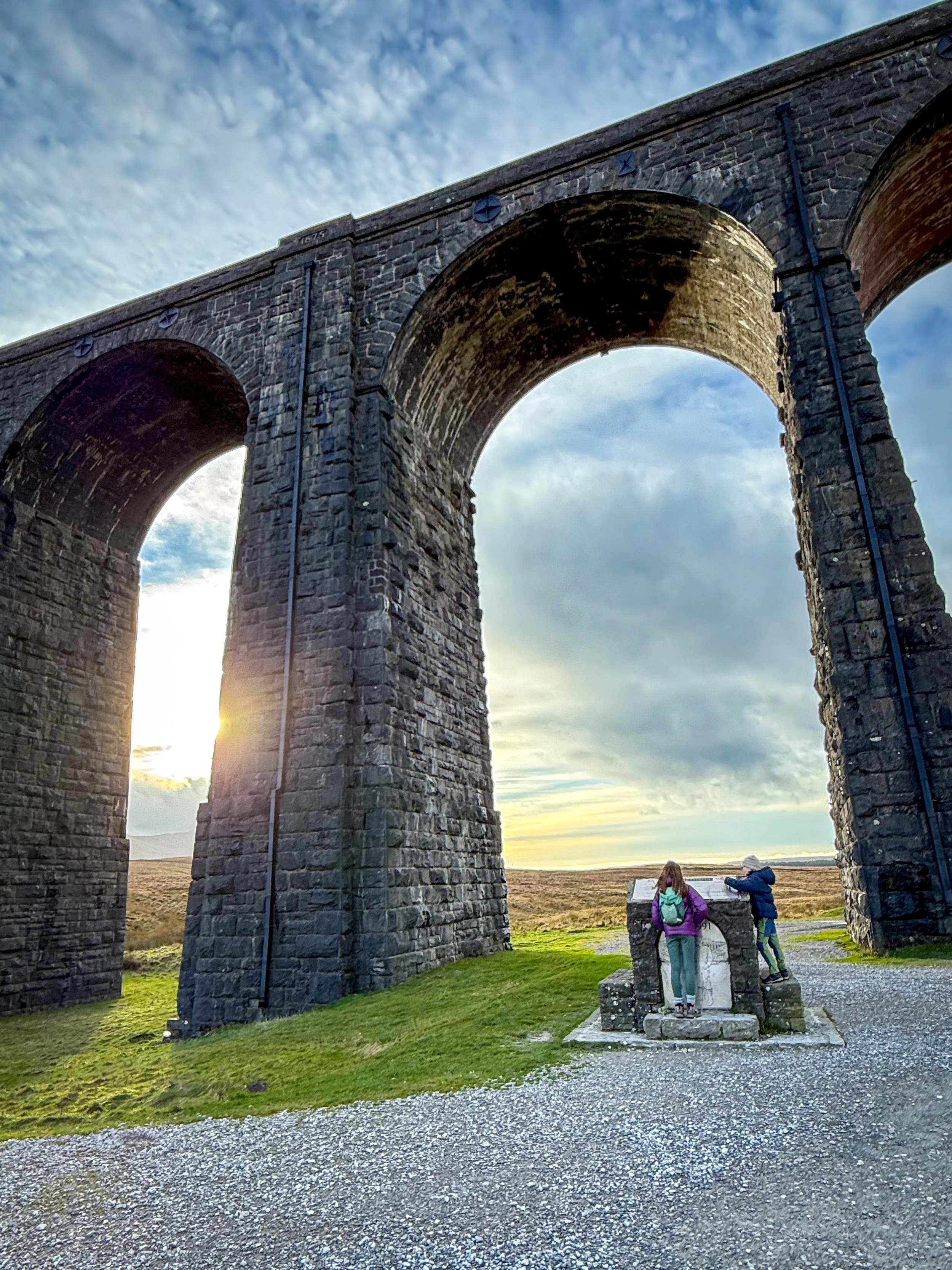 The ribblehead viaduct with the sunset in the background and children looking at monument