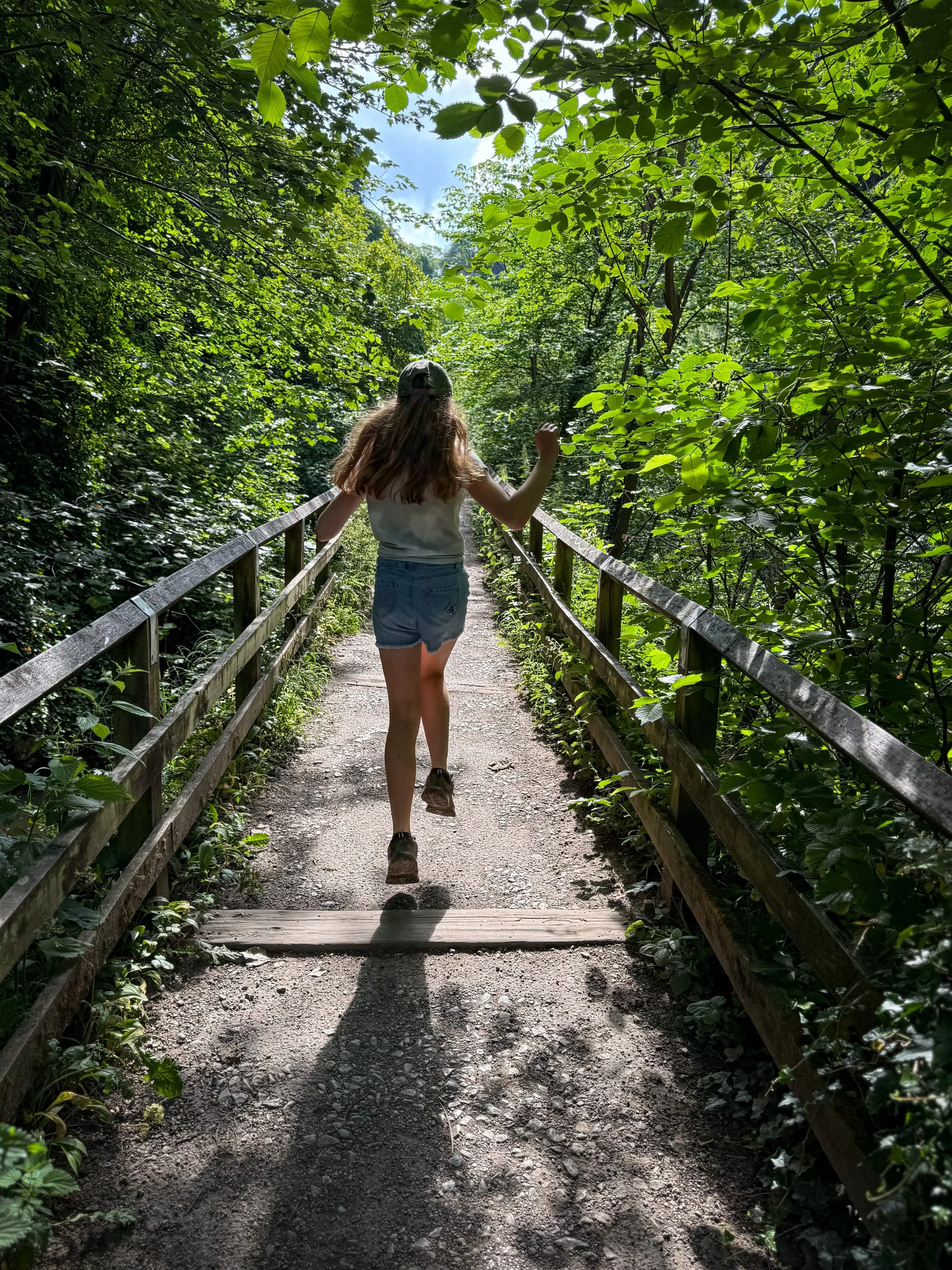 Child running through woods on a fenced path in the sun