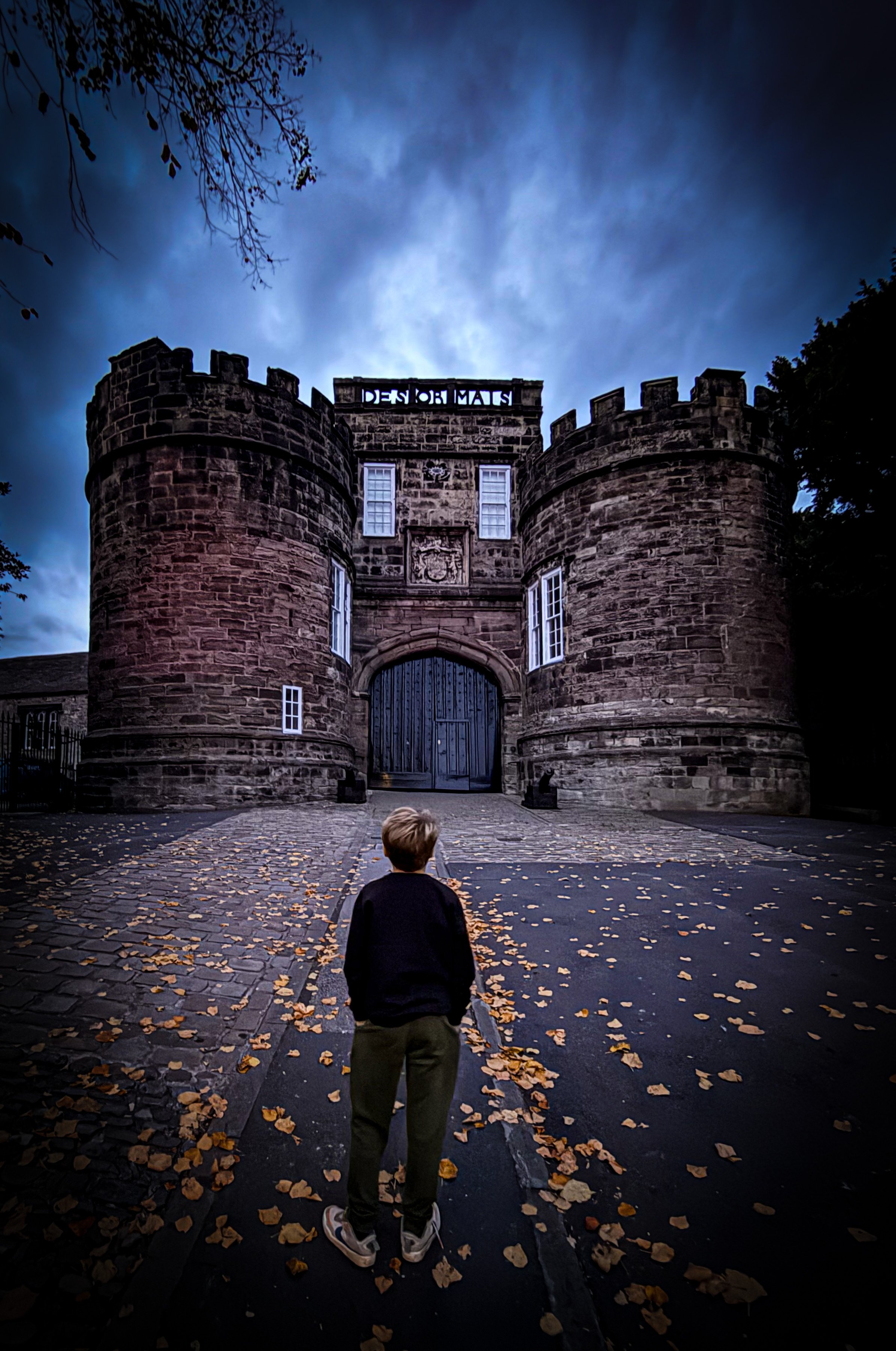 Child walking towards a dark castle at night with moody dark skies and cobbled street