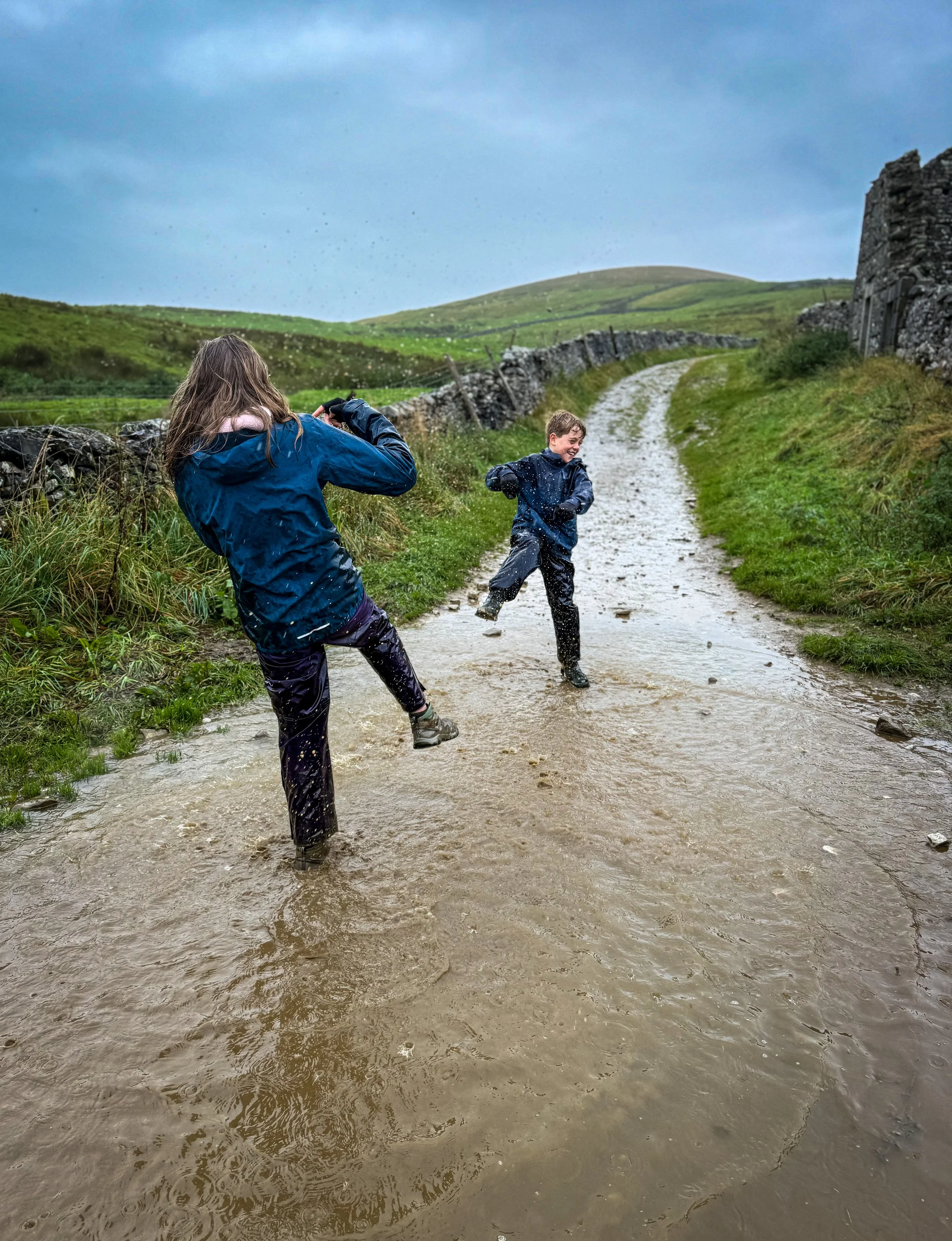Children playing in a puddle in the rain kicking water