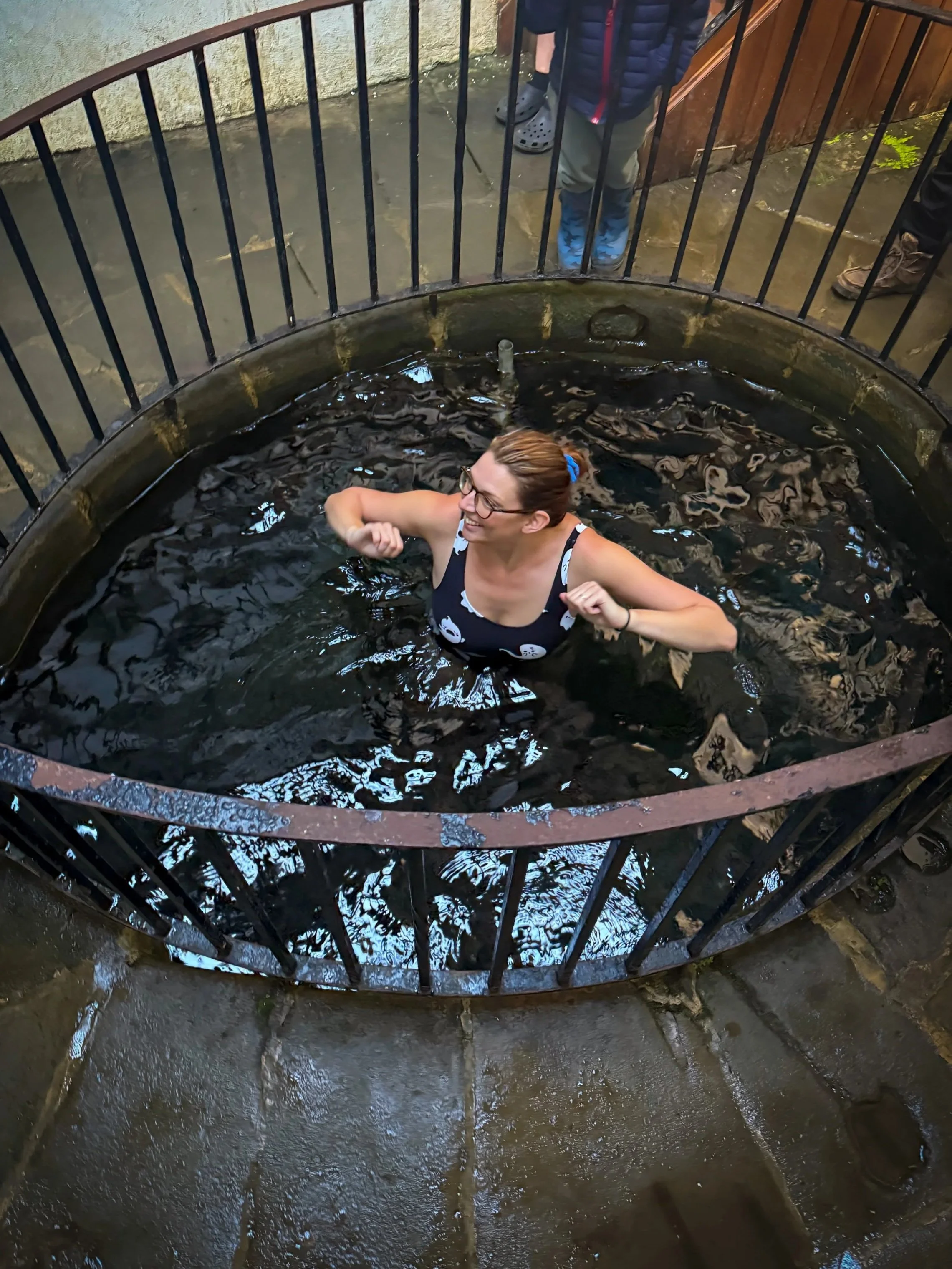 Woman in a stone lined spa pool surrounded by iron railings