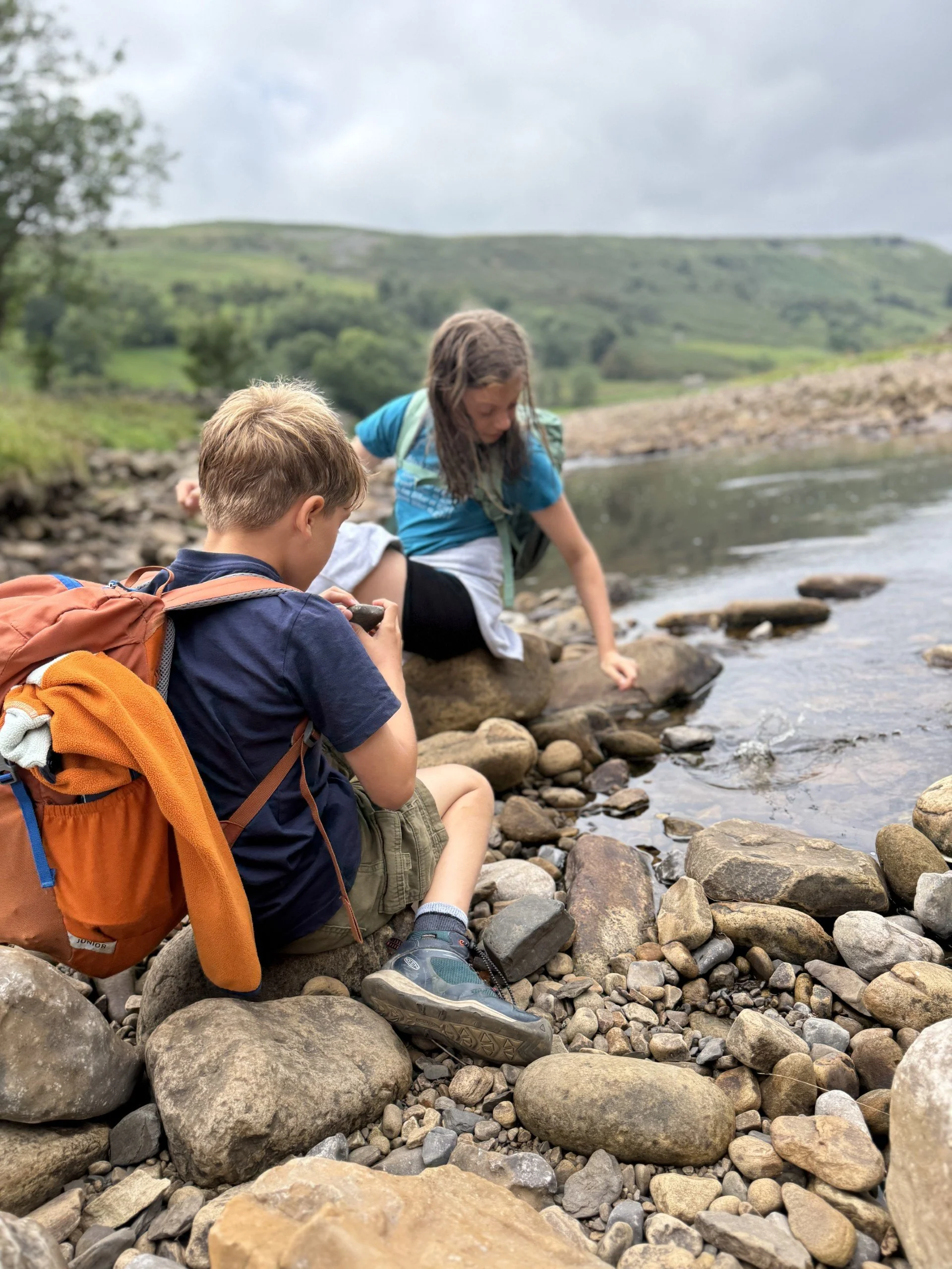 Two children sat by a river searching through rocks