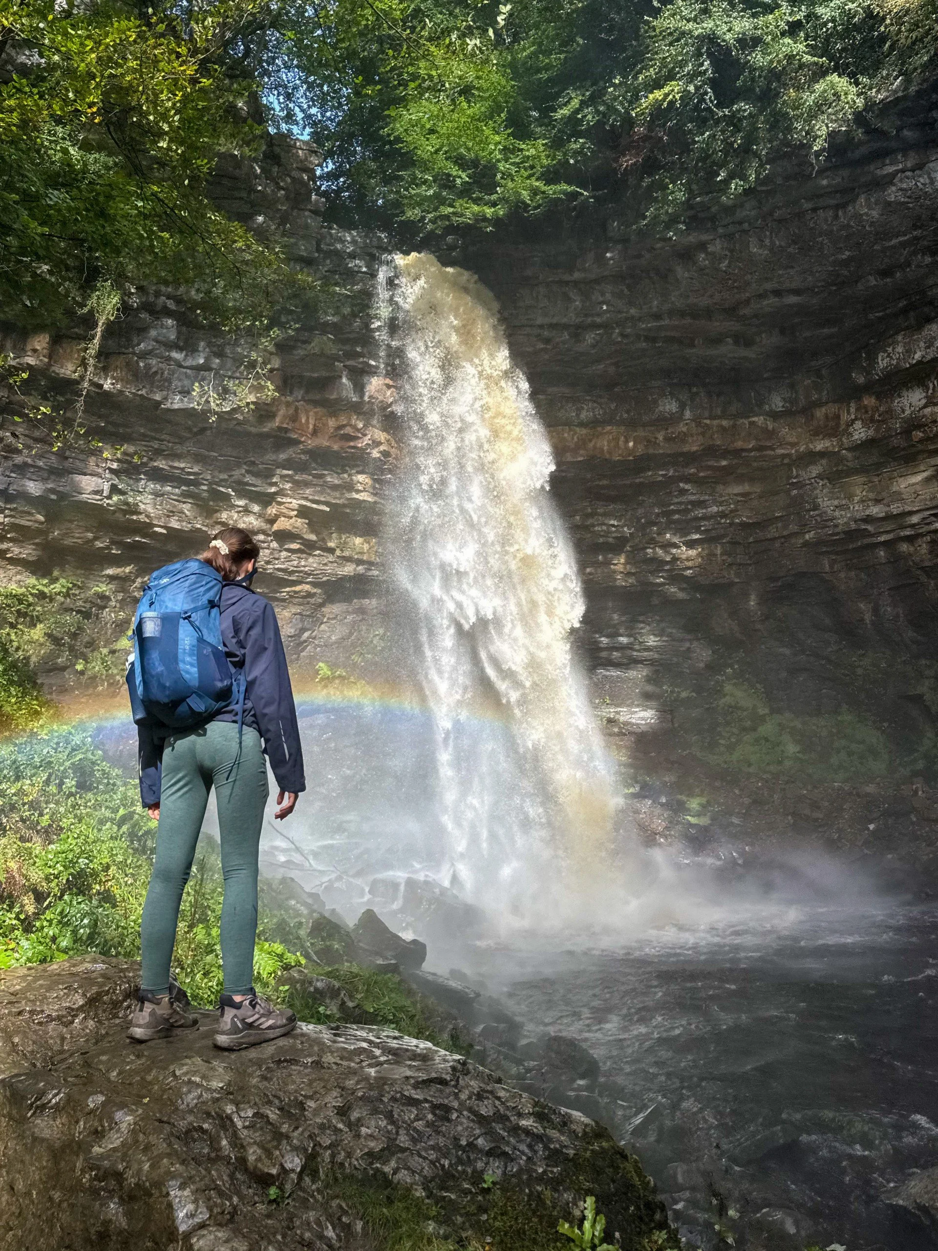 Child standing at a huge waterfall in spate with a rainbow