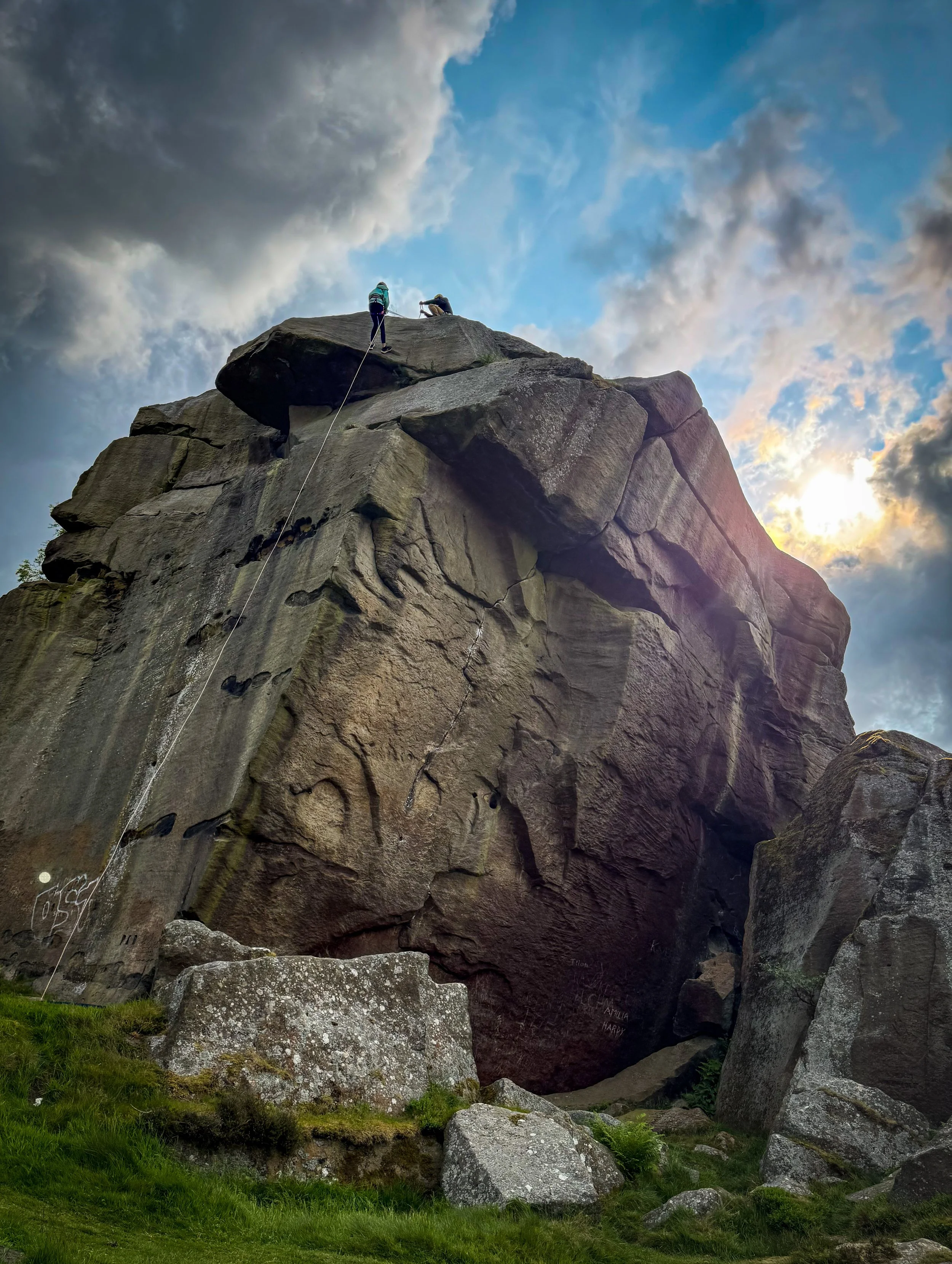Child rappelling off a large rock face with another person on the rope under blue skies