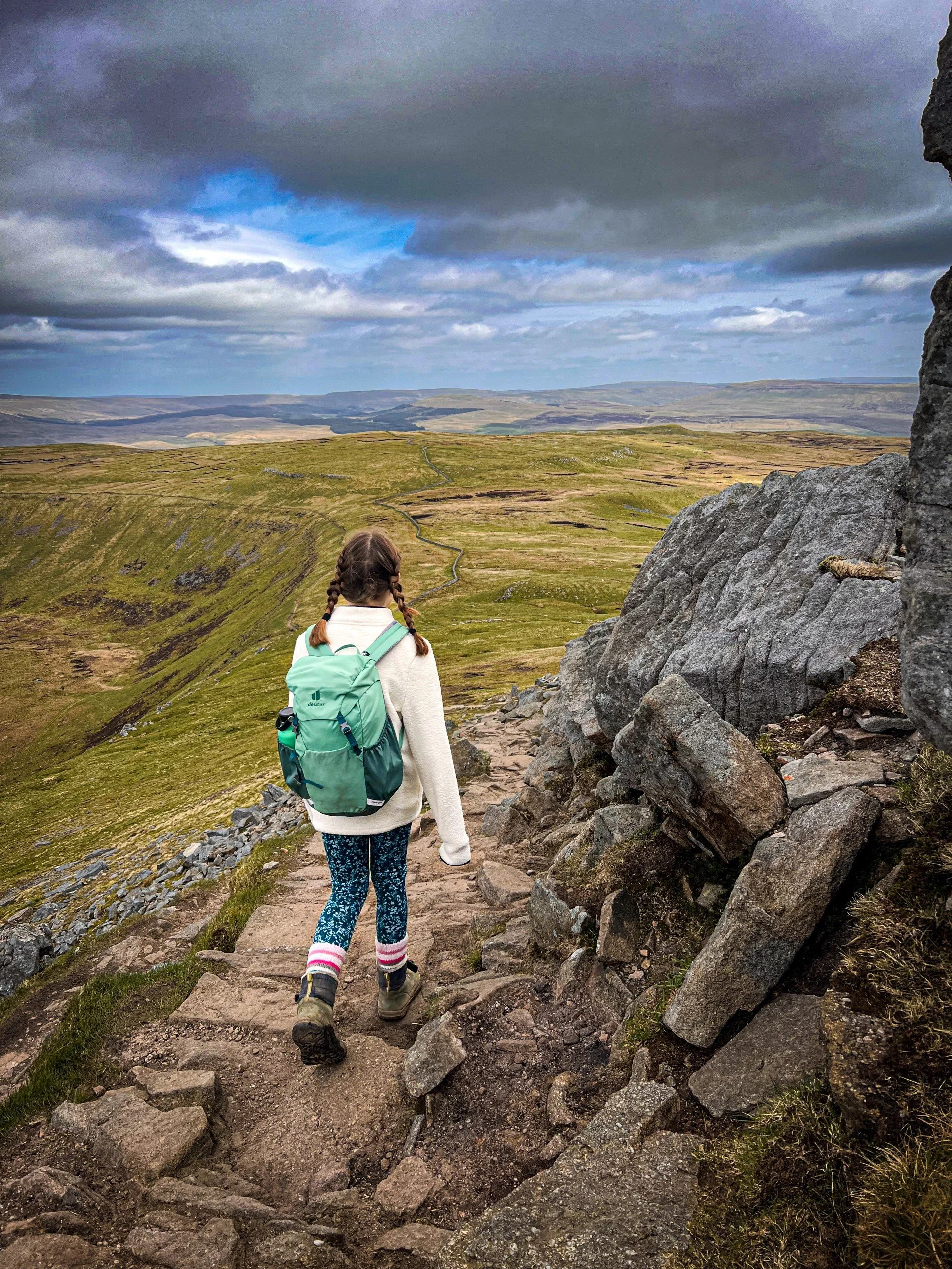 Child walking around exposed mountain edge with plateau beyond