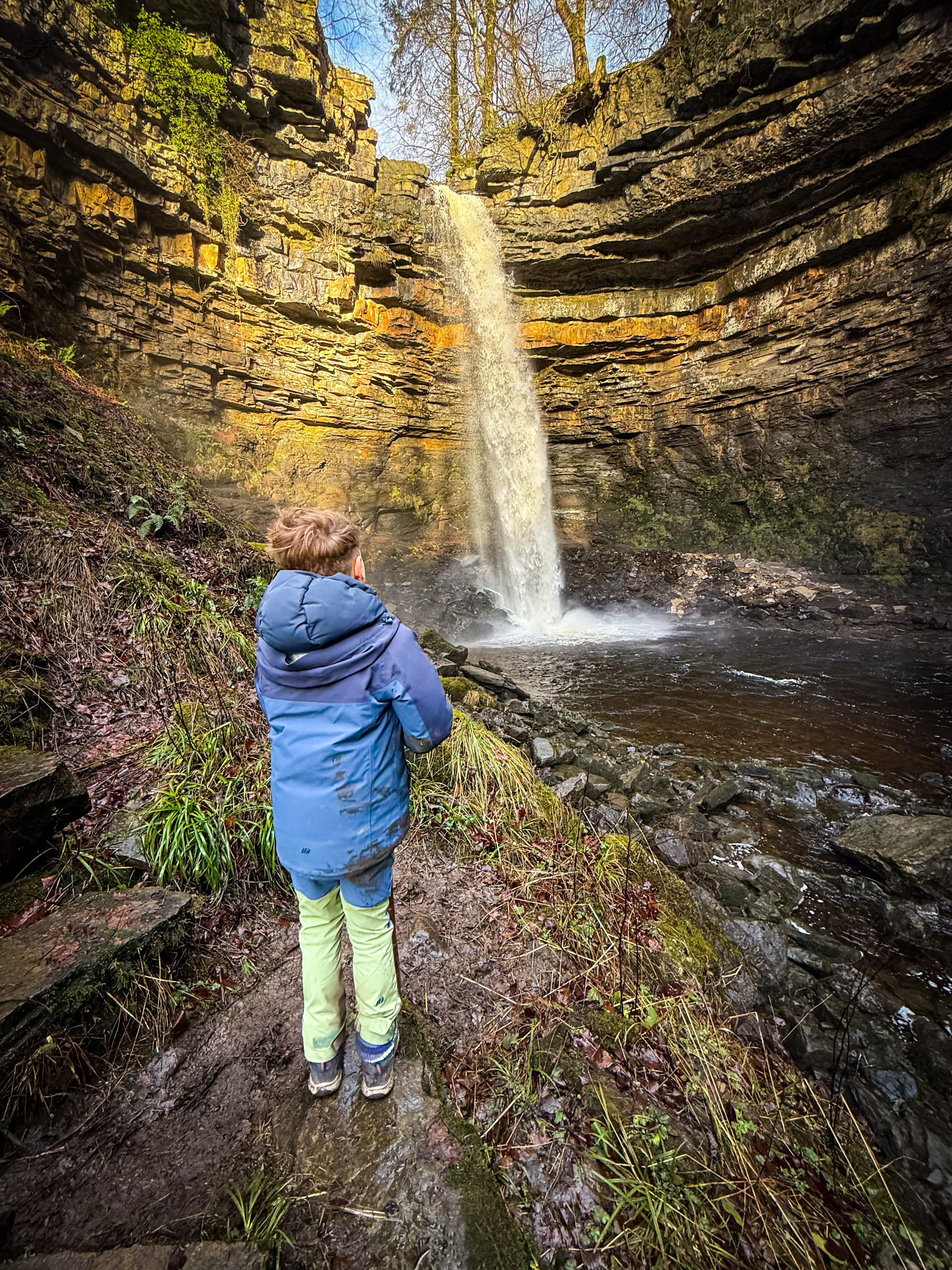 Child standing in front of the tallest waterfall in England with blue skies and rocky sides
