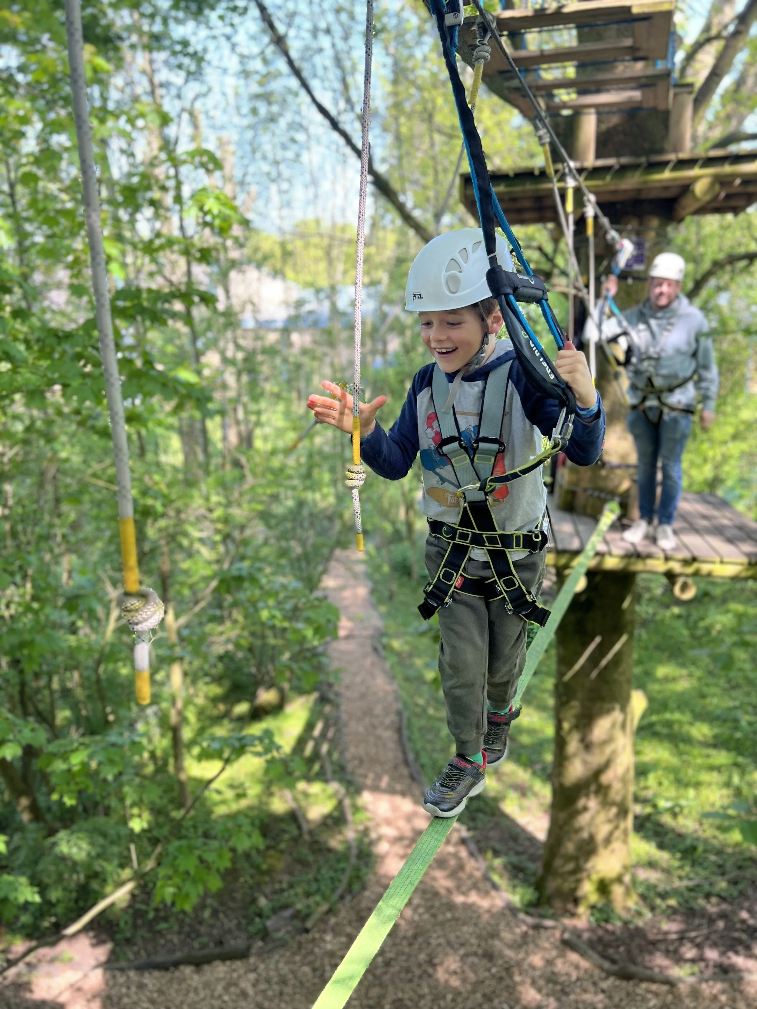 Child walking along high ropes course in trees with helmet