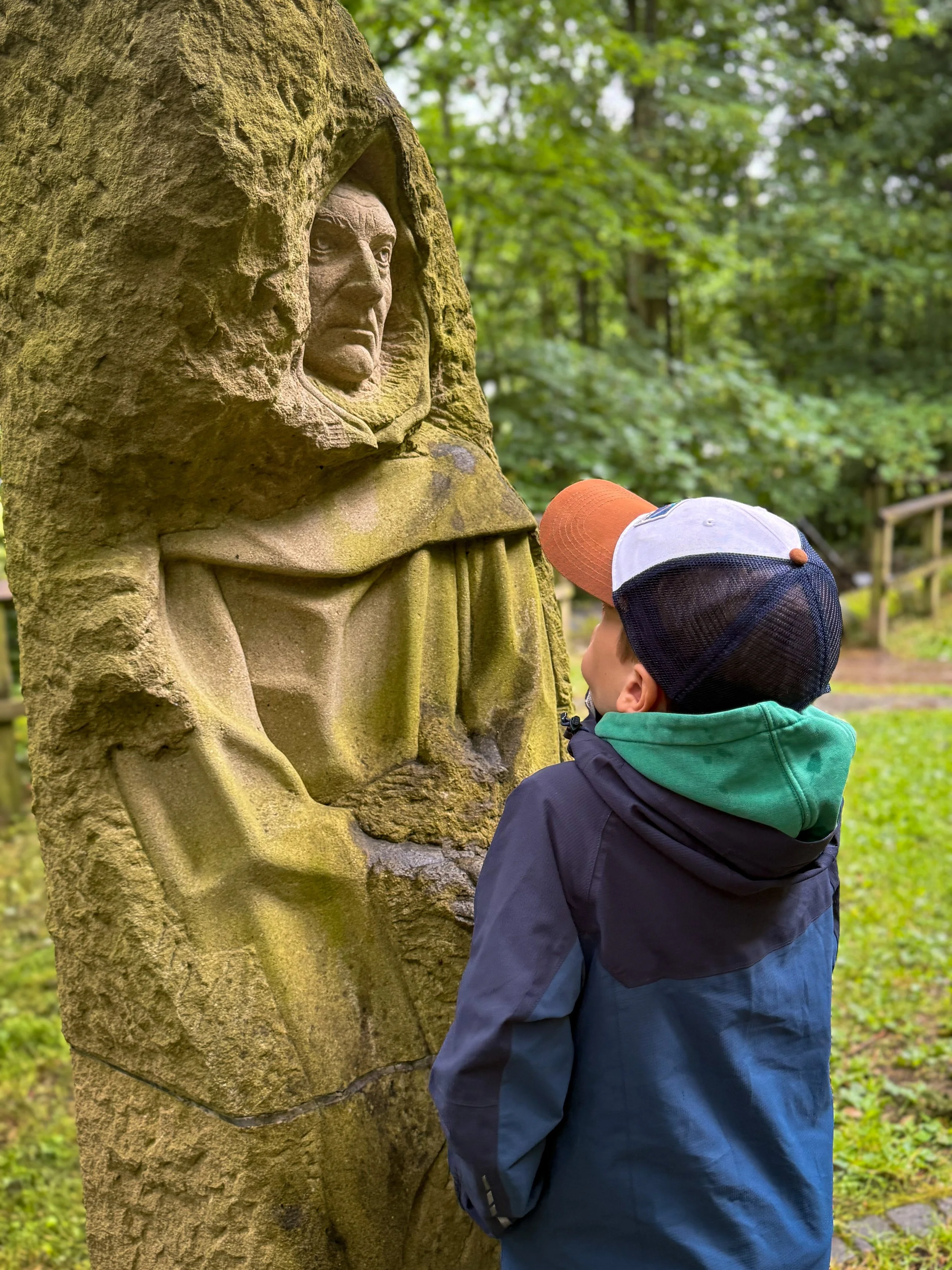 Child looking at a stone statue of a monk wearing a robe and hood