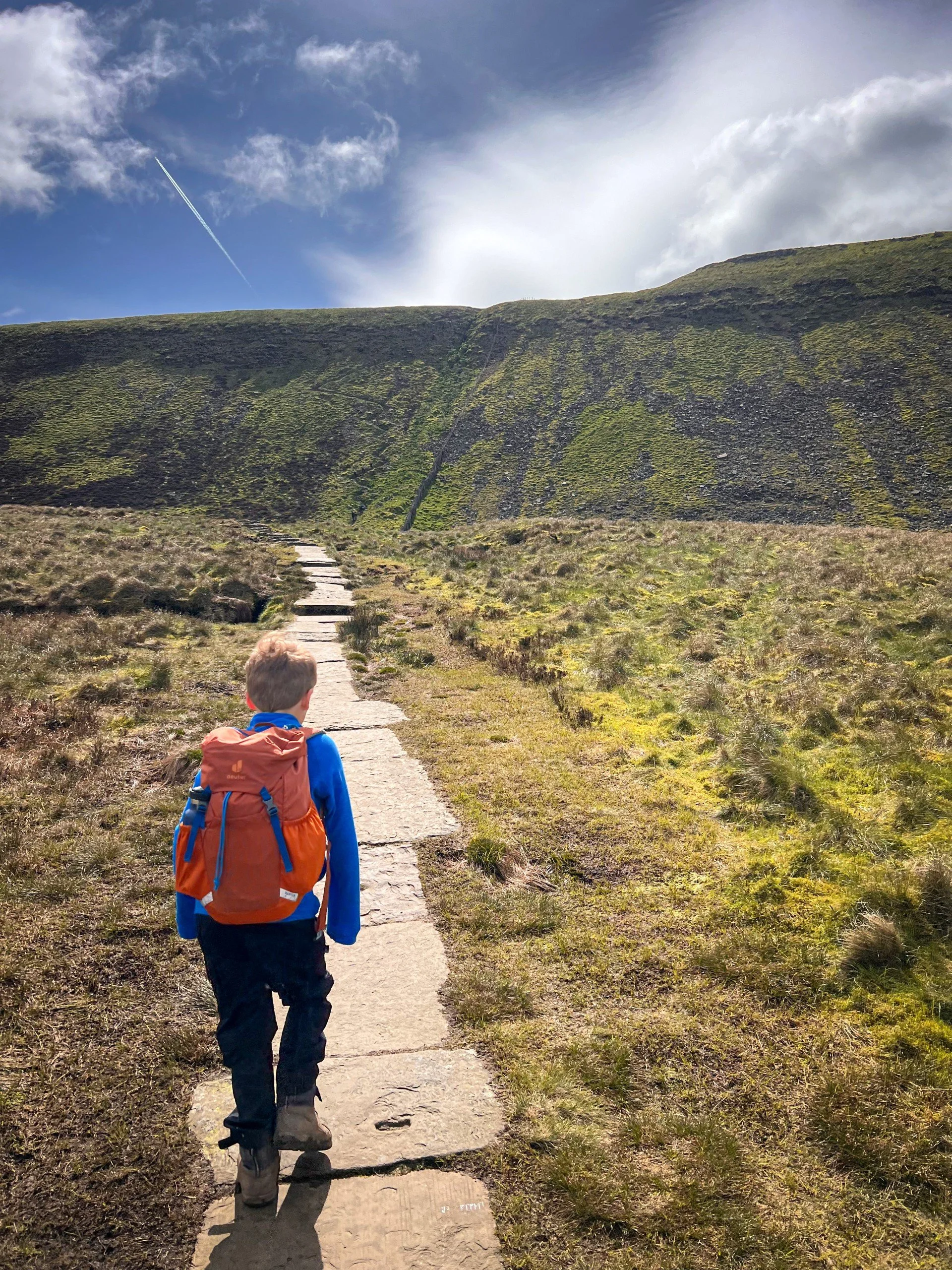 Child walking along flagged path in sunshine with steep mountain side ahead