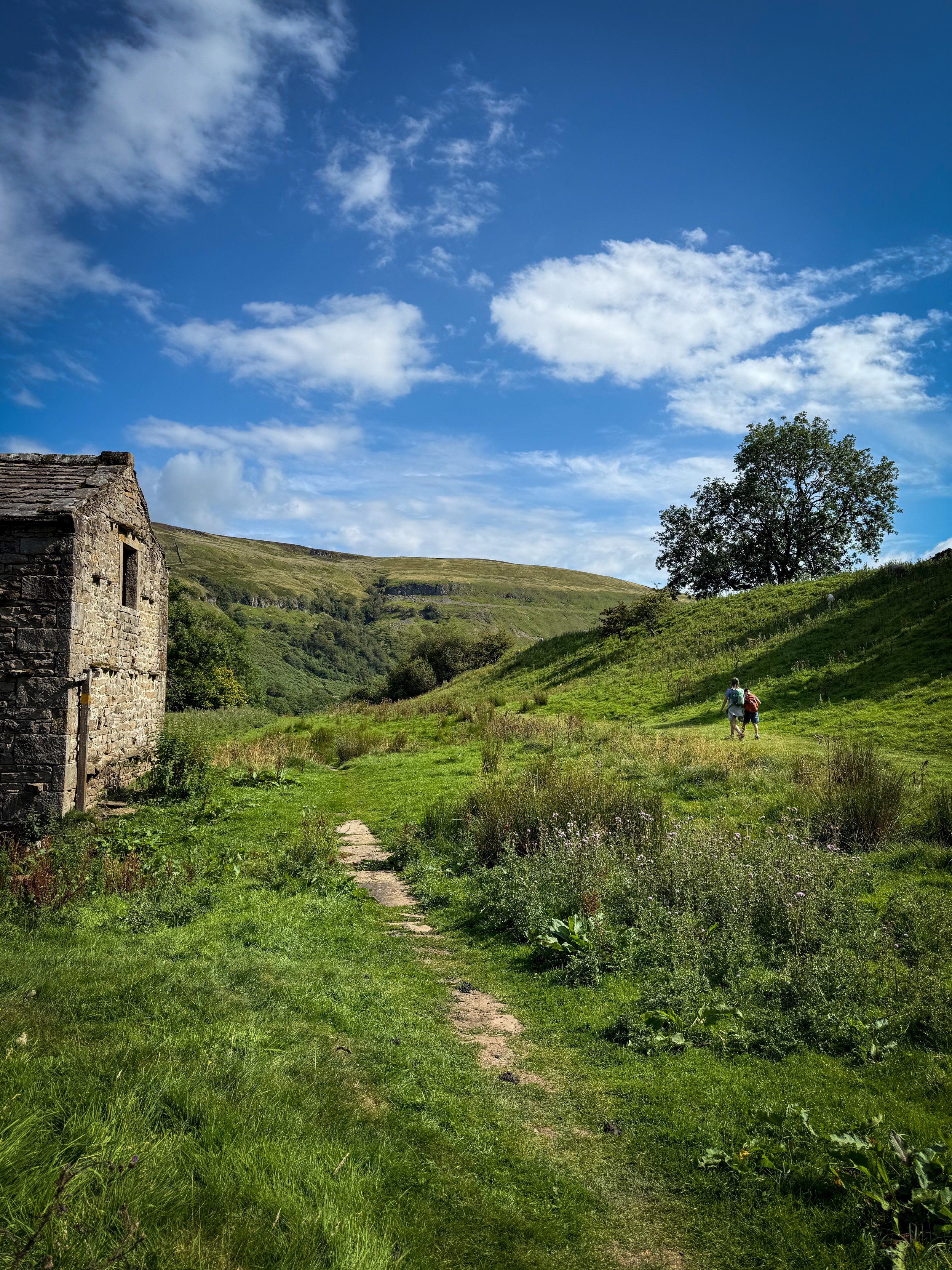 A ruin of a farmhouse with child walking alongside under blue summer skies in the countryside