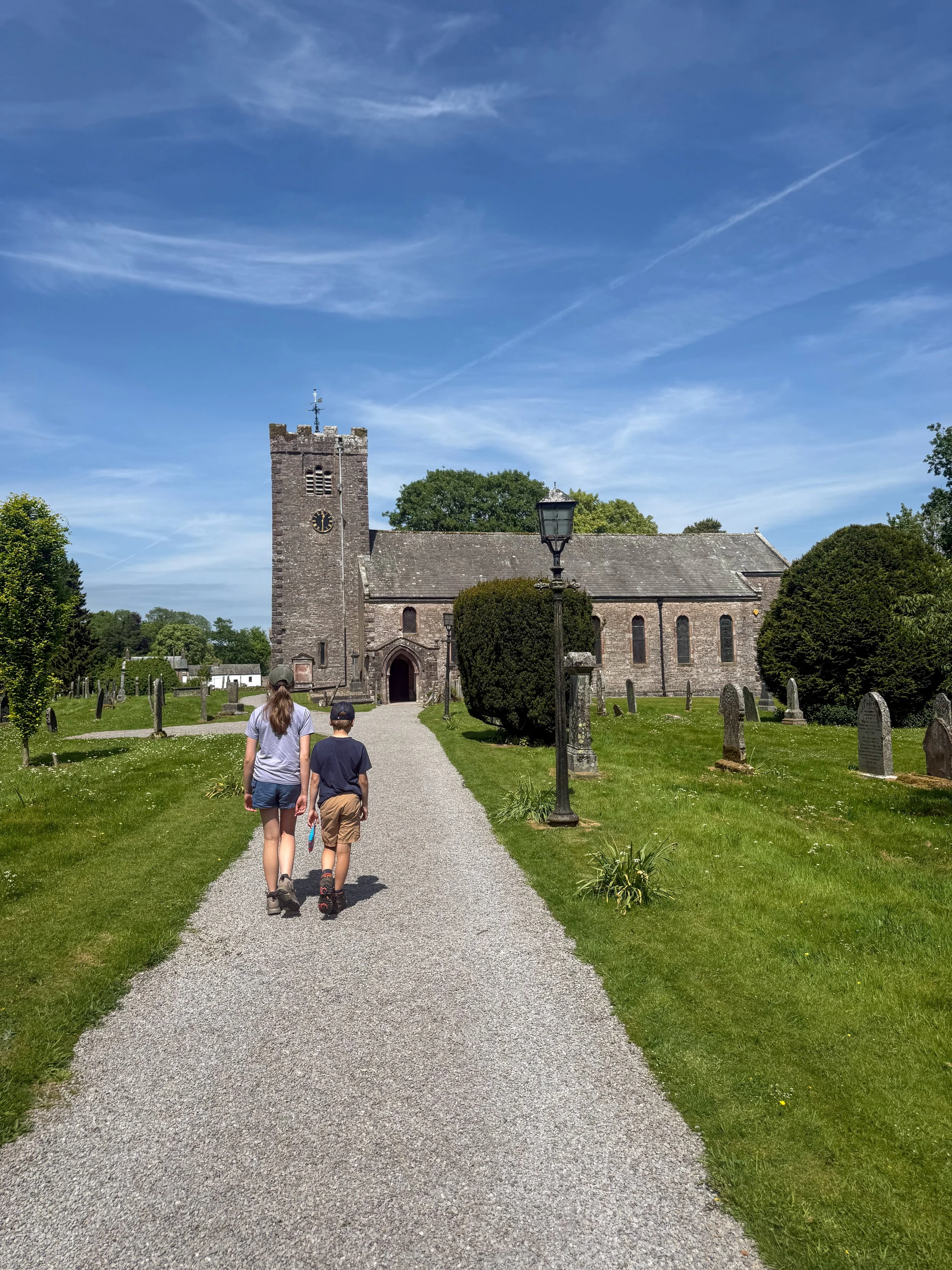 Two children walking down a church path towards a church under a blue sky in summer