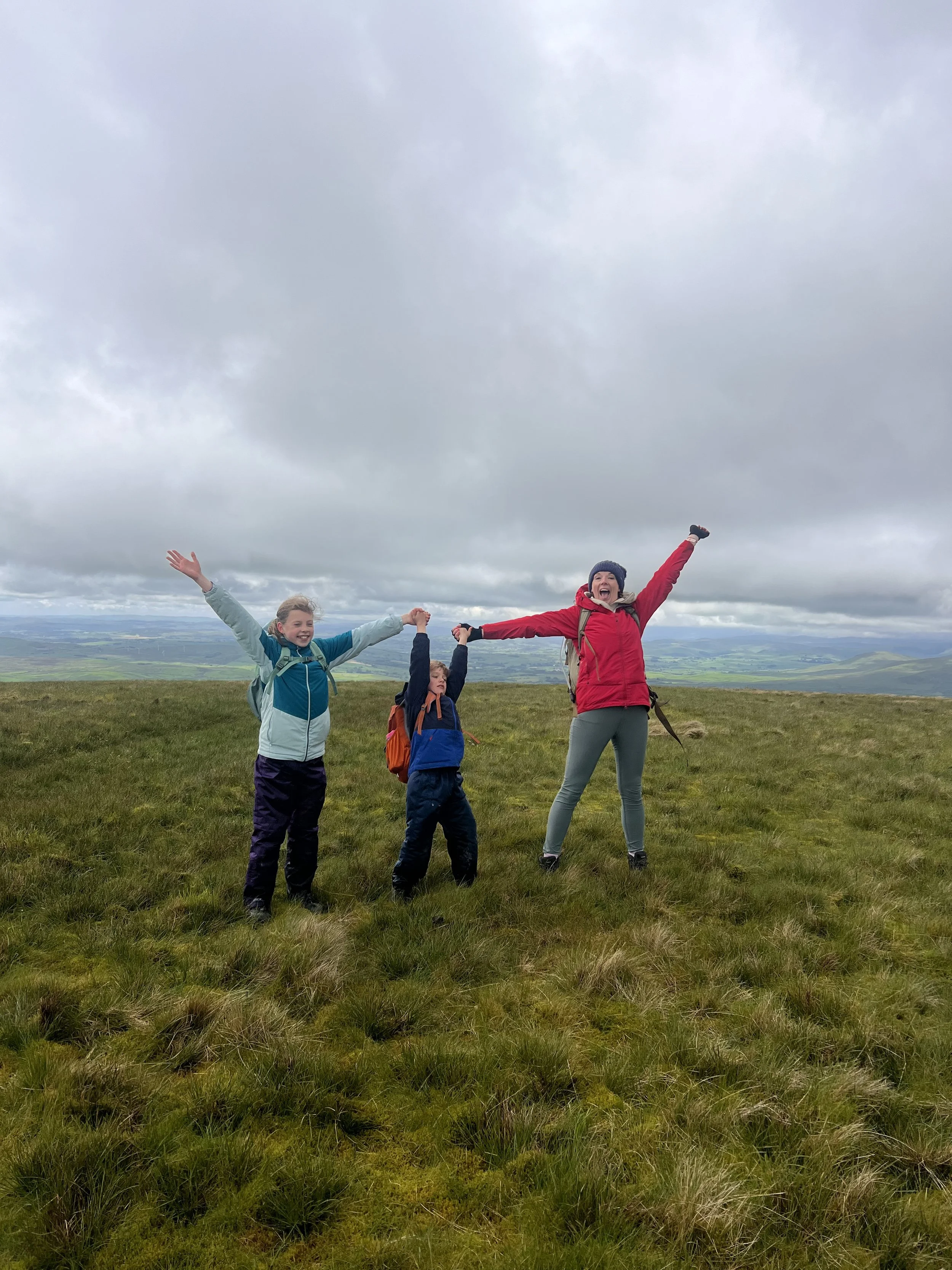 Mum and two children standing on top of a grassy moor with arms up
