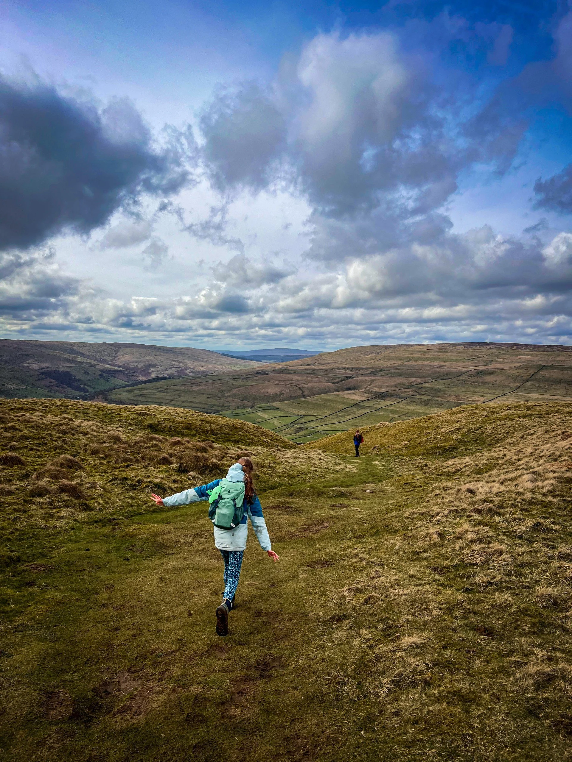 Two children with arms out running down a slope with views of mountains ahead