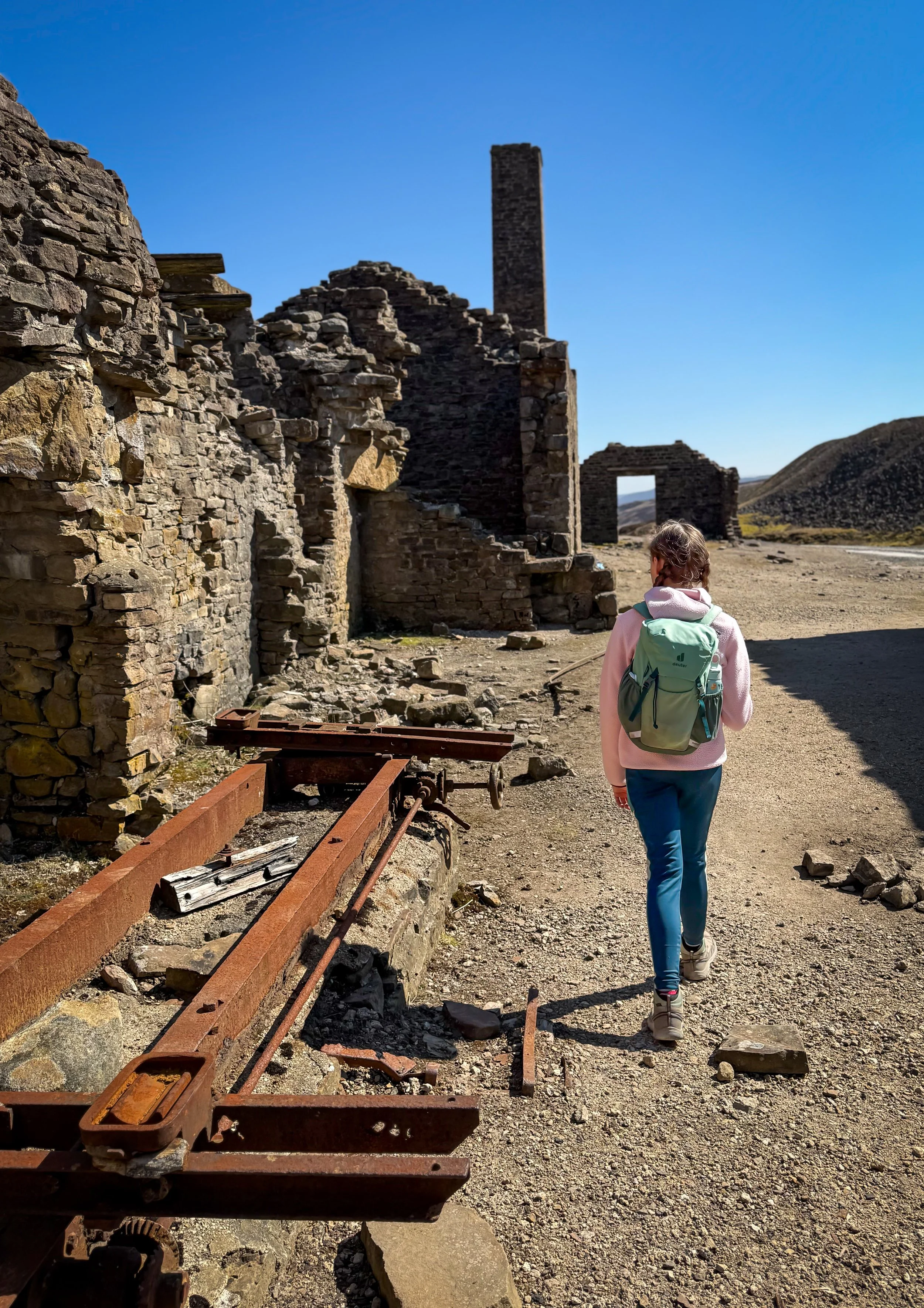 Child walking through the ruins of a smelt mill with rusty machinery and a large chimney