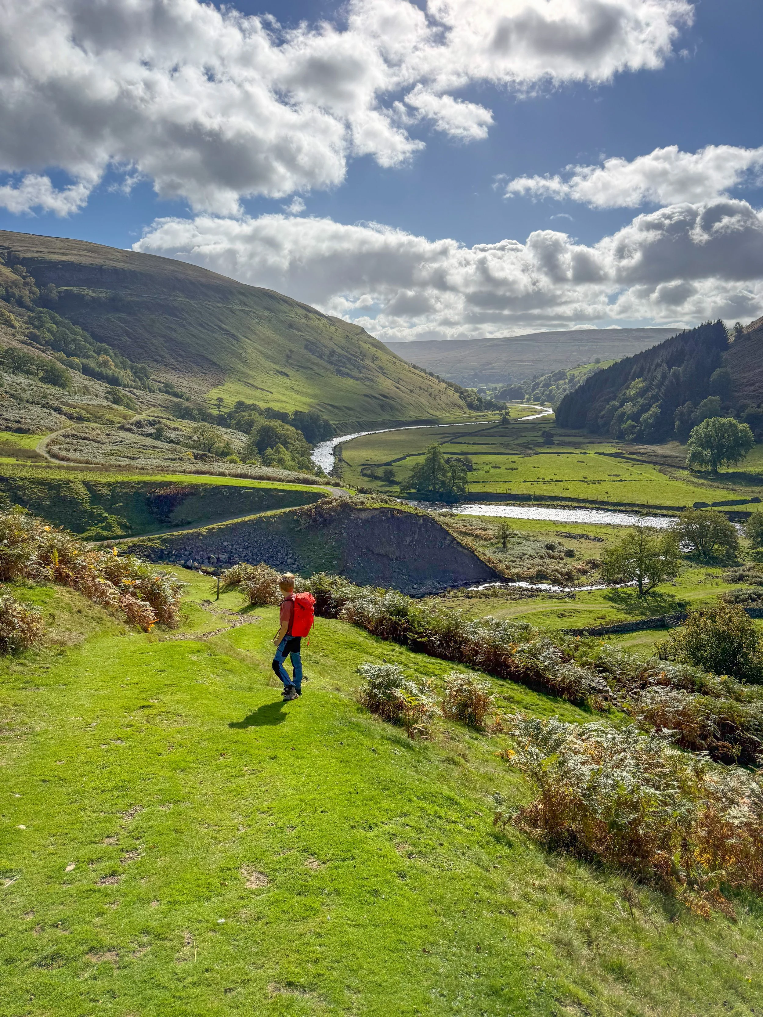 Child standing in an elevated position over a valley floor with hills either side and a river reflecting the sun as it snakes through