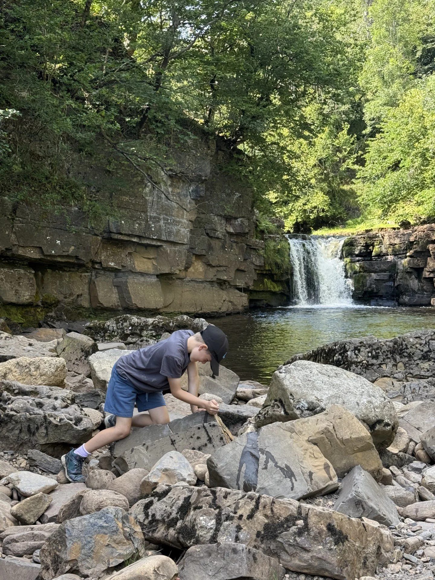 Child finding fossils in rocks on the edge of a waterfall in a deep rocky basin