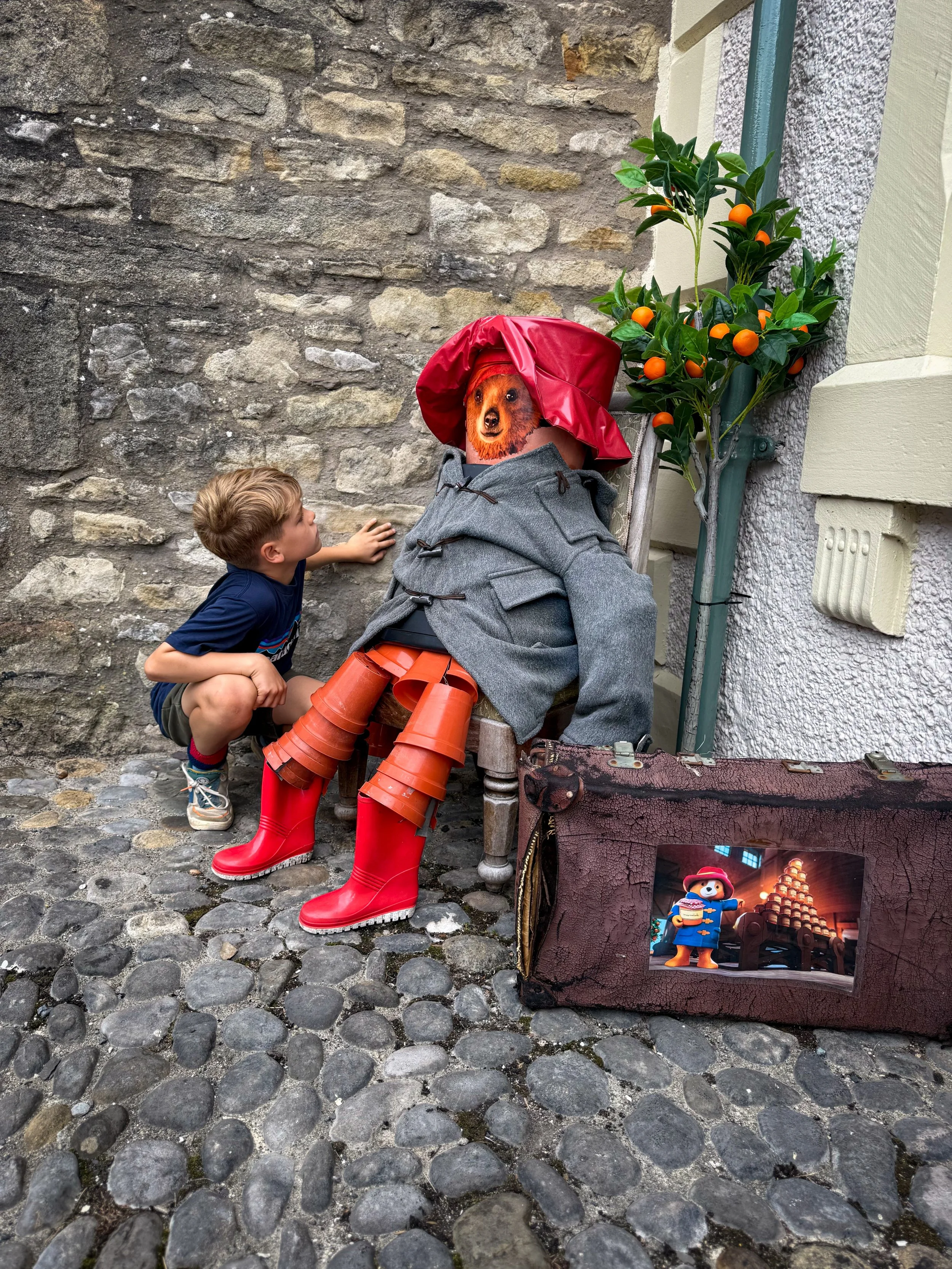 Child crouched next to a paddington bear made out of flowerpots