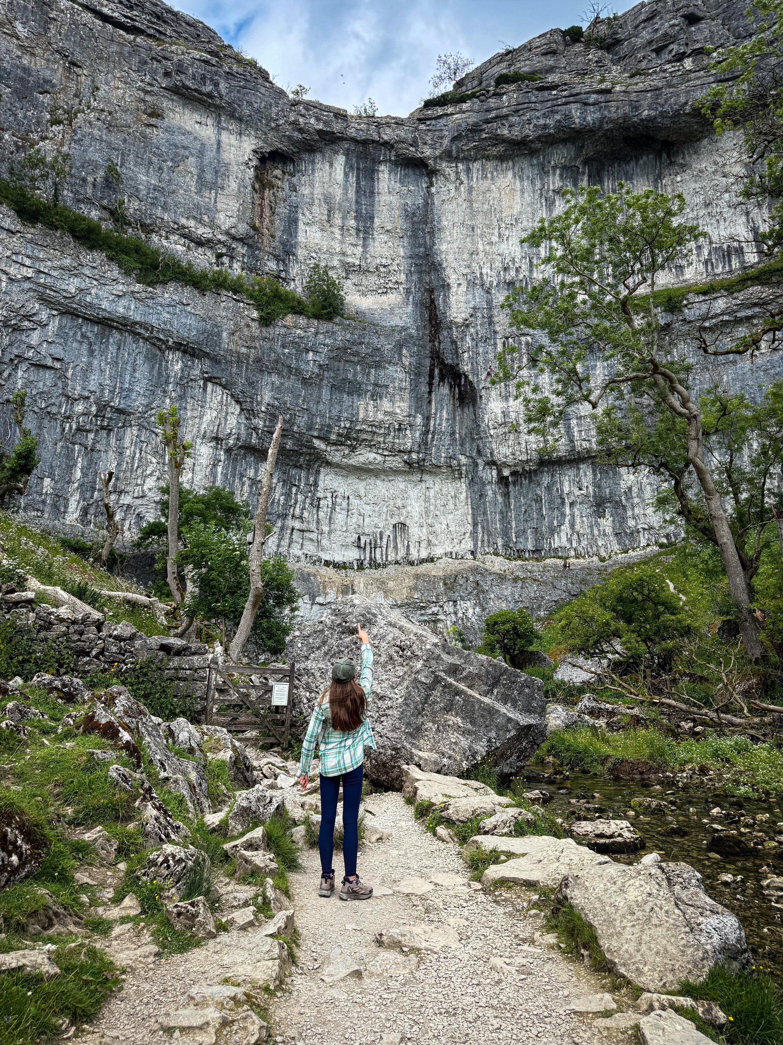 Child standing pointing up at a rocky cove face surrounded by trees and bushes