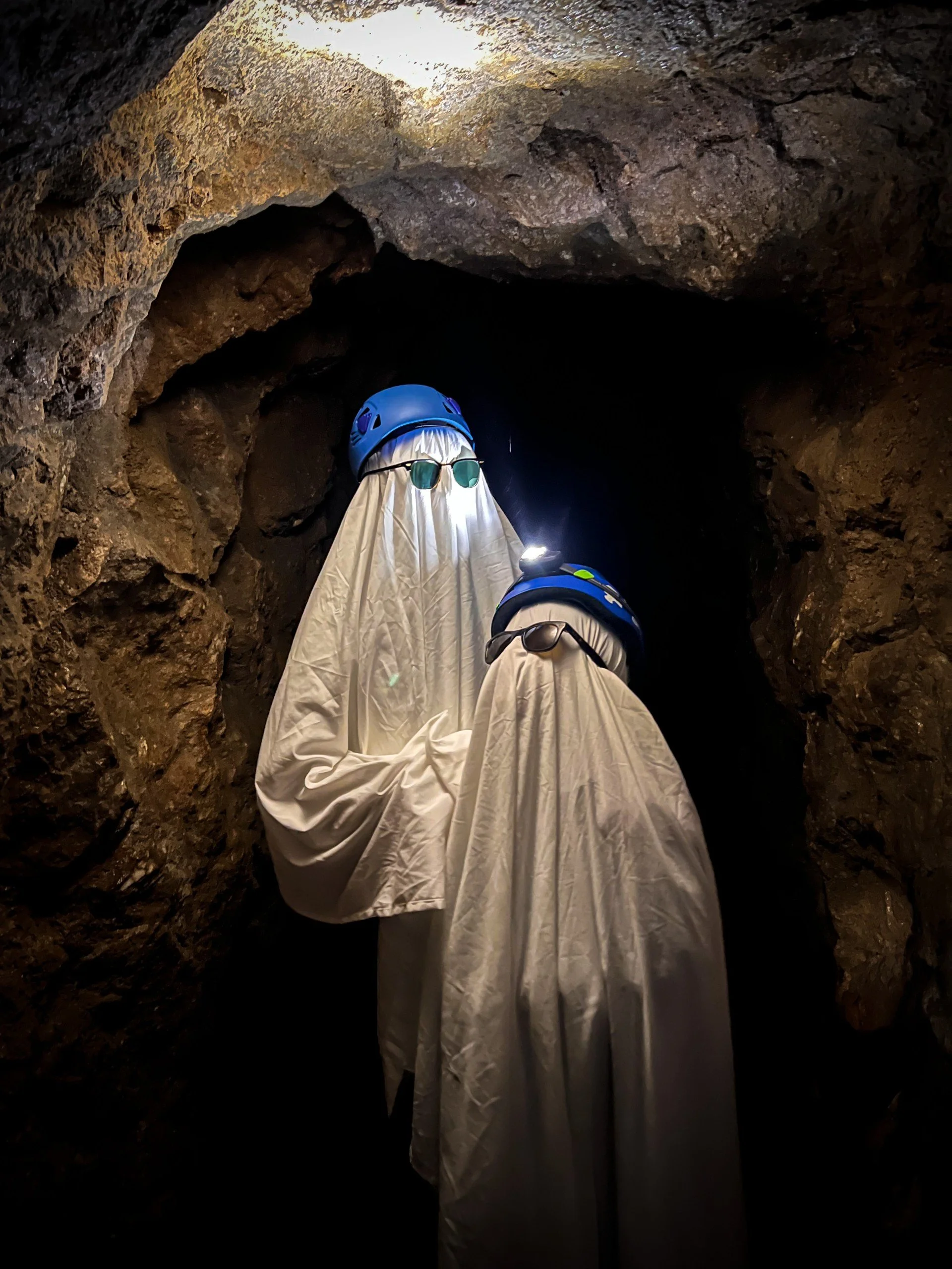 Two children wearing white sheets and caving helmets with sunglasses and a headtorch dressed as ghosts