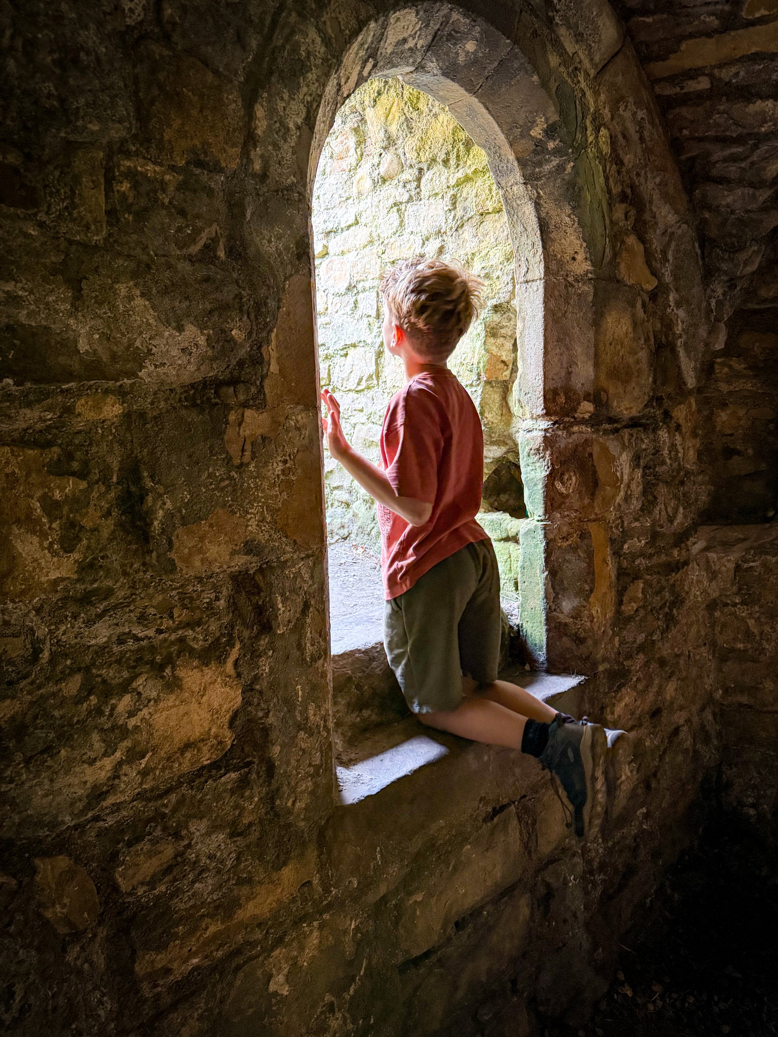 A child sat on a windowsill of an old abbey ruin with sun coming in
