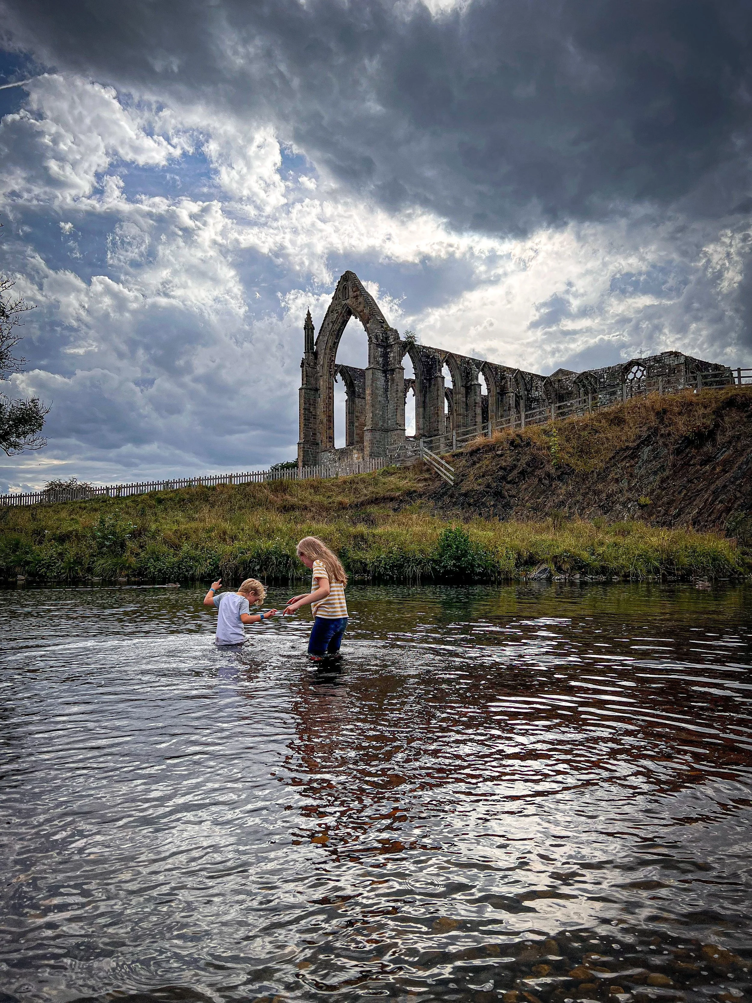 Children paddling in the river with ruins of an abbey behind