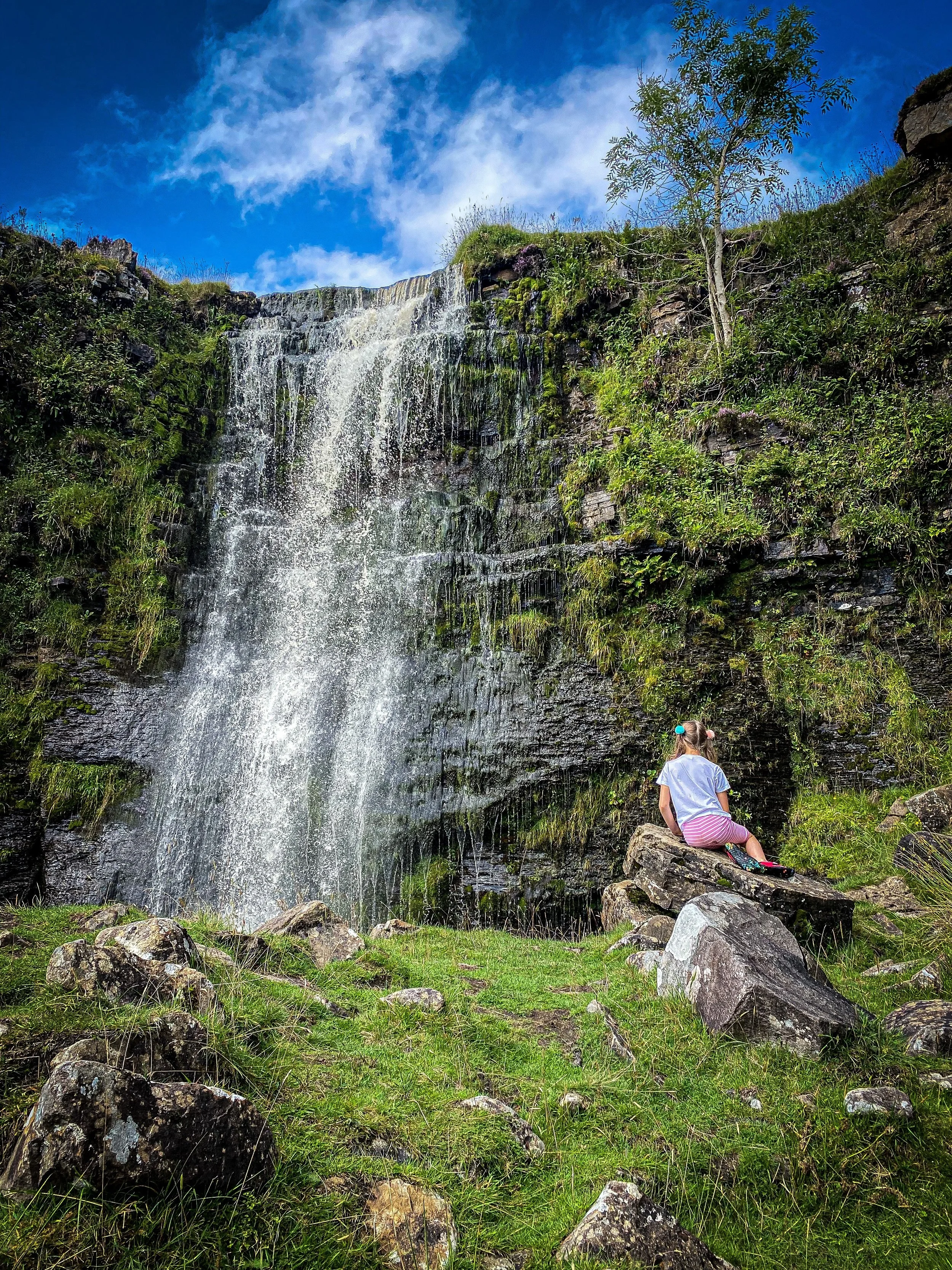 Force Gill waterfall with a child next to it sat on a rock under blue sky