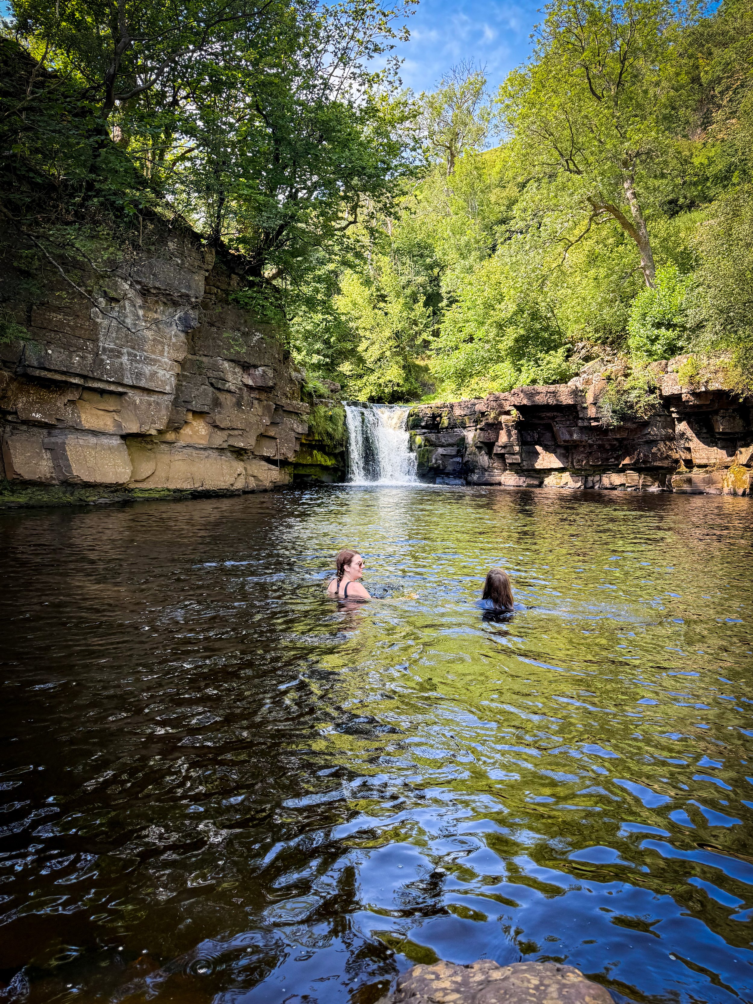 mum and daughter wild swimming in a waterfall in summer