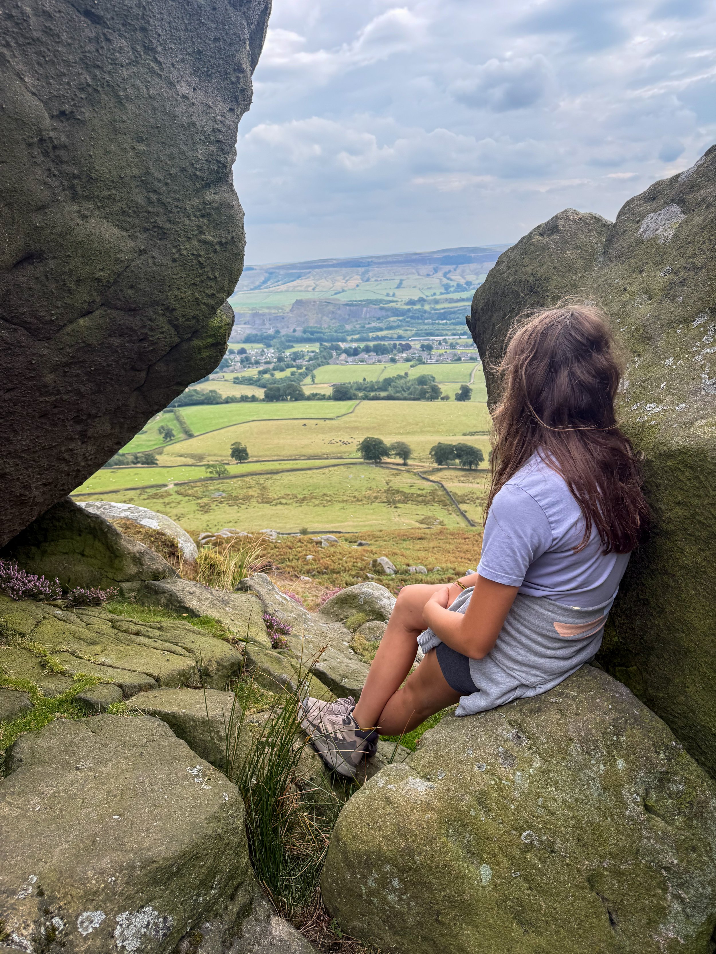 Child sitting on a rock looking out towards views of green trees and fields beyond