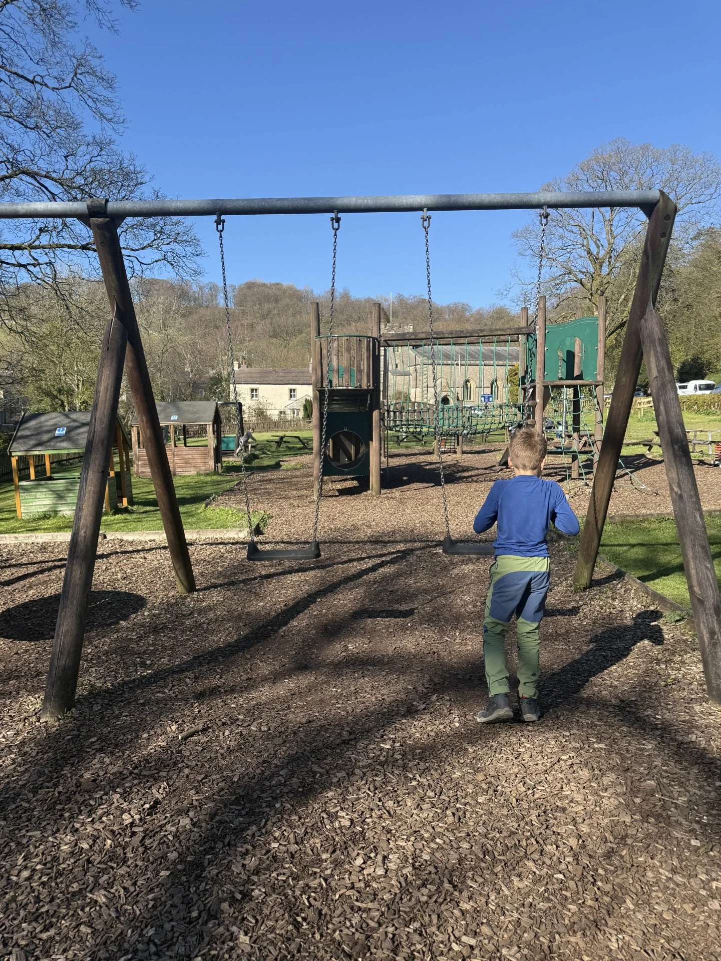 Child going to the swings in Clapham playpark with climbing frame behind