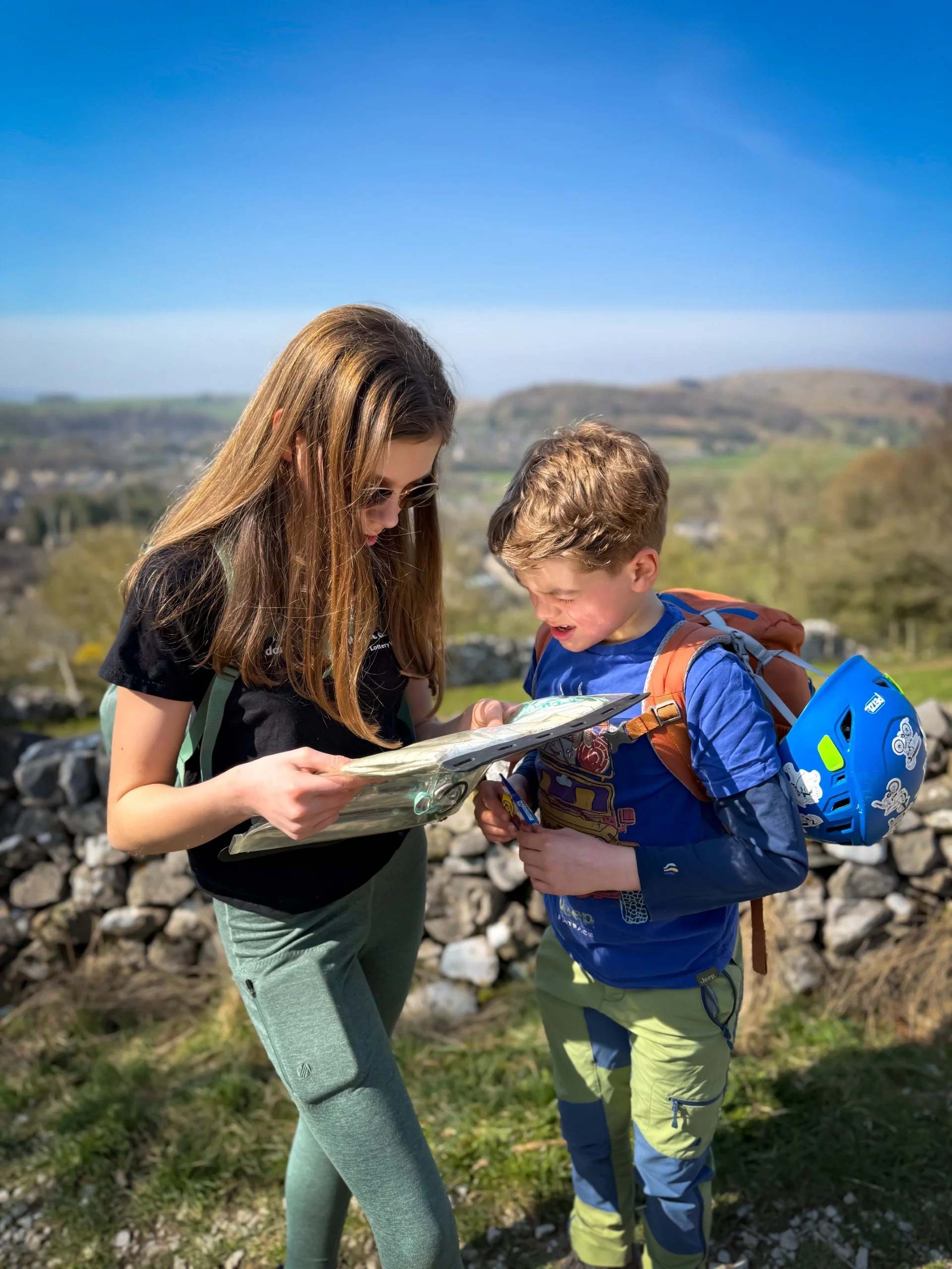 Two children reading a map with blue skies and hills in the background