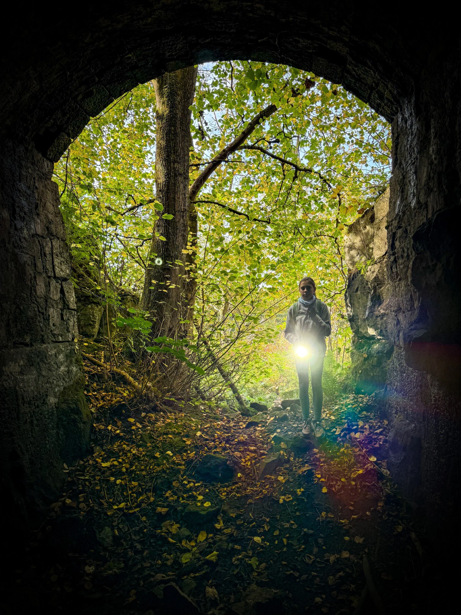 Child standing in the mouth of a large kiln with a torch and autumn leaves in the background