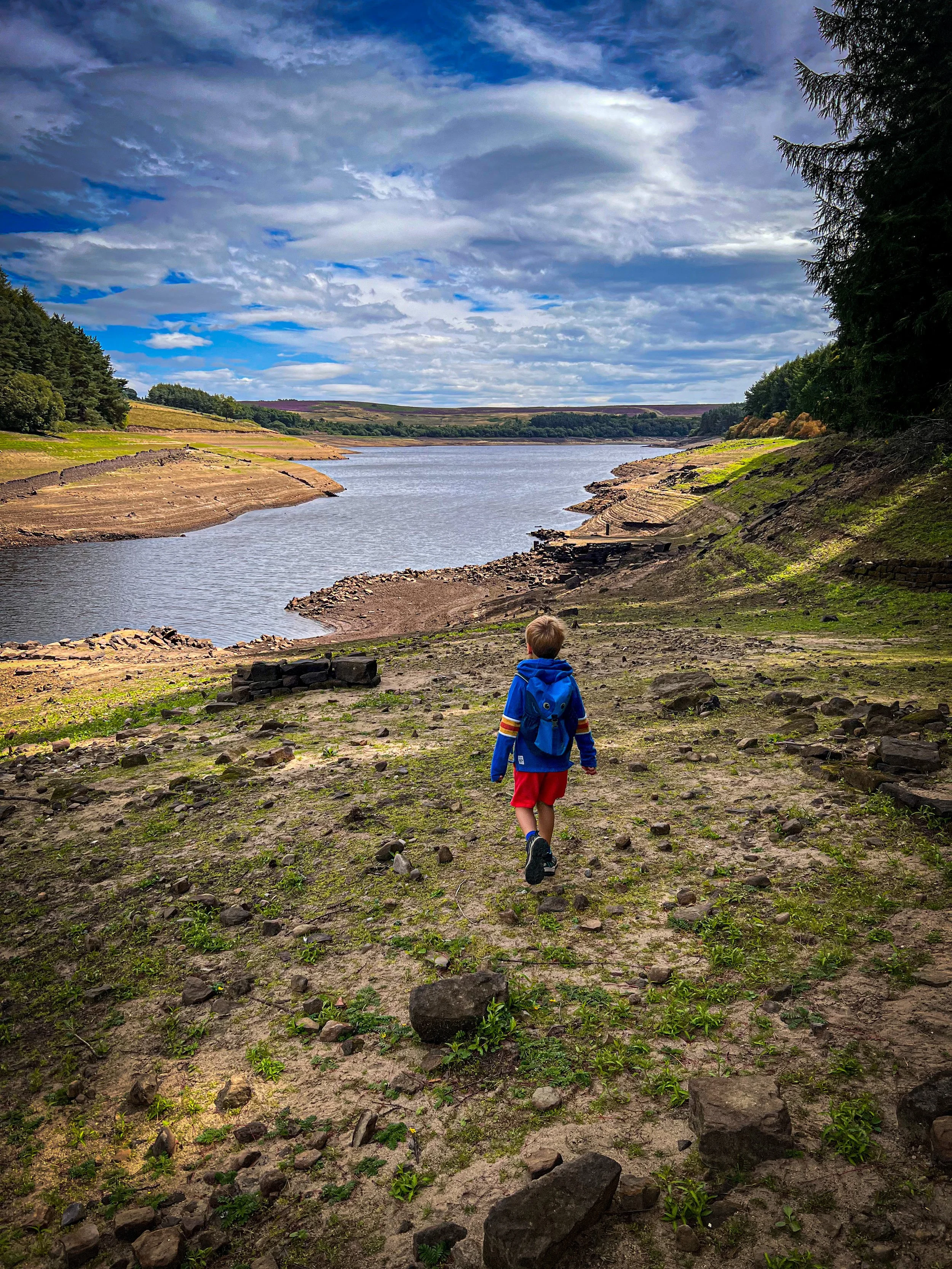 Child walking towards a reservoir which is drying up with ruins poking out the water