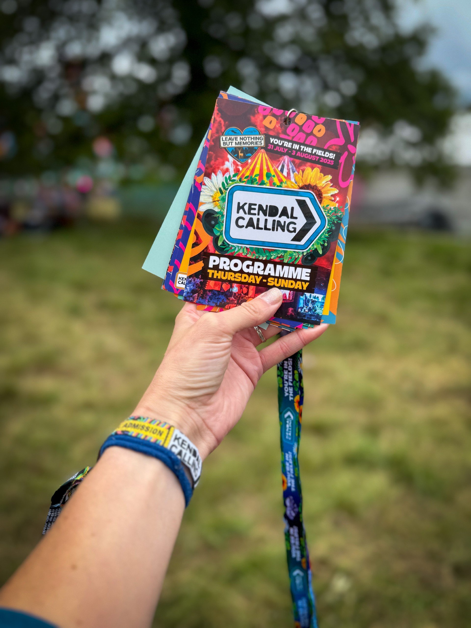 A hand holding a kendal calling lanyard with a timetable on it for 2025