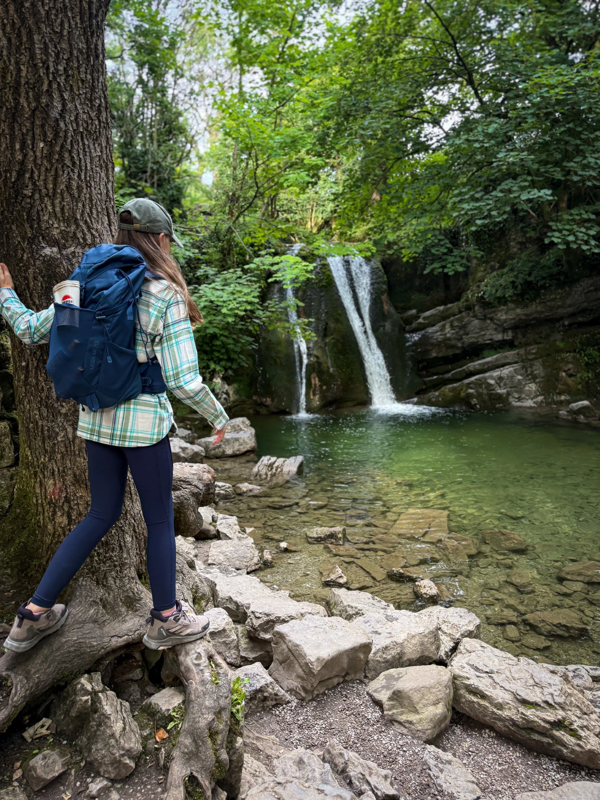 Child leaning against a tree with a waterfall ahead in wooded gorge