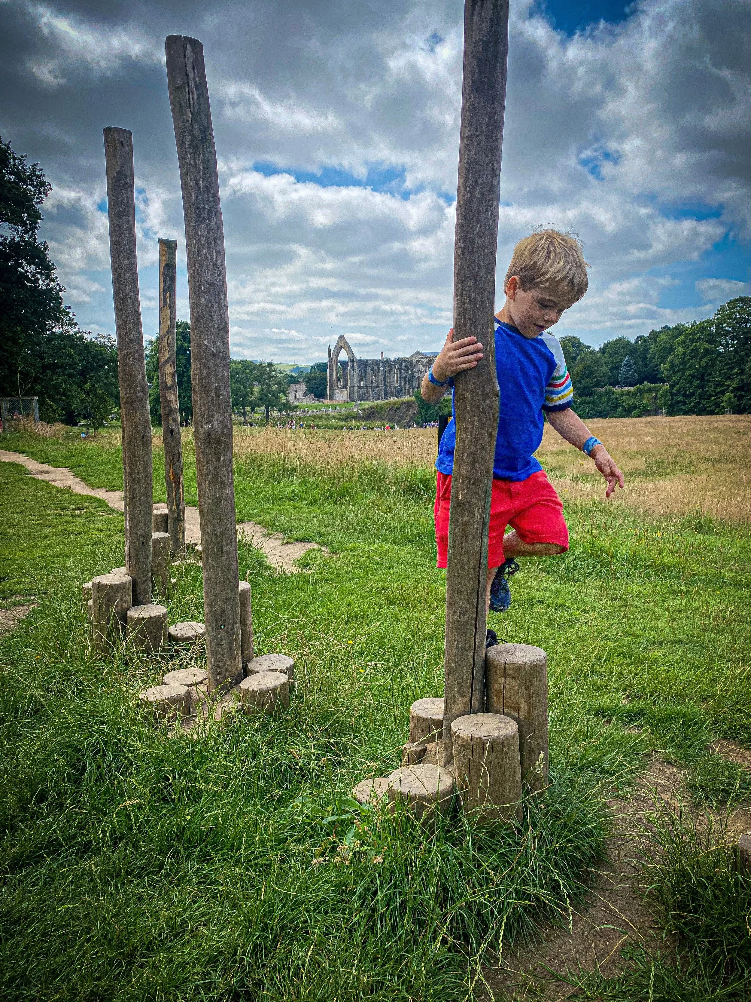 Child doing an obstacle course at Bolton Abbey with ruins of the priory in the background