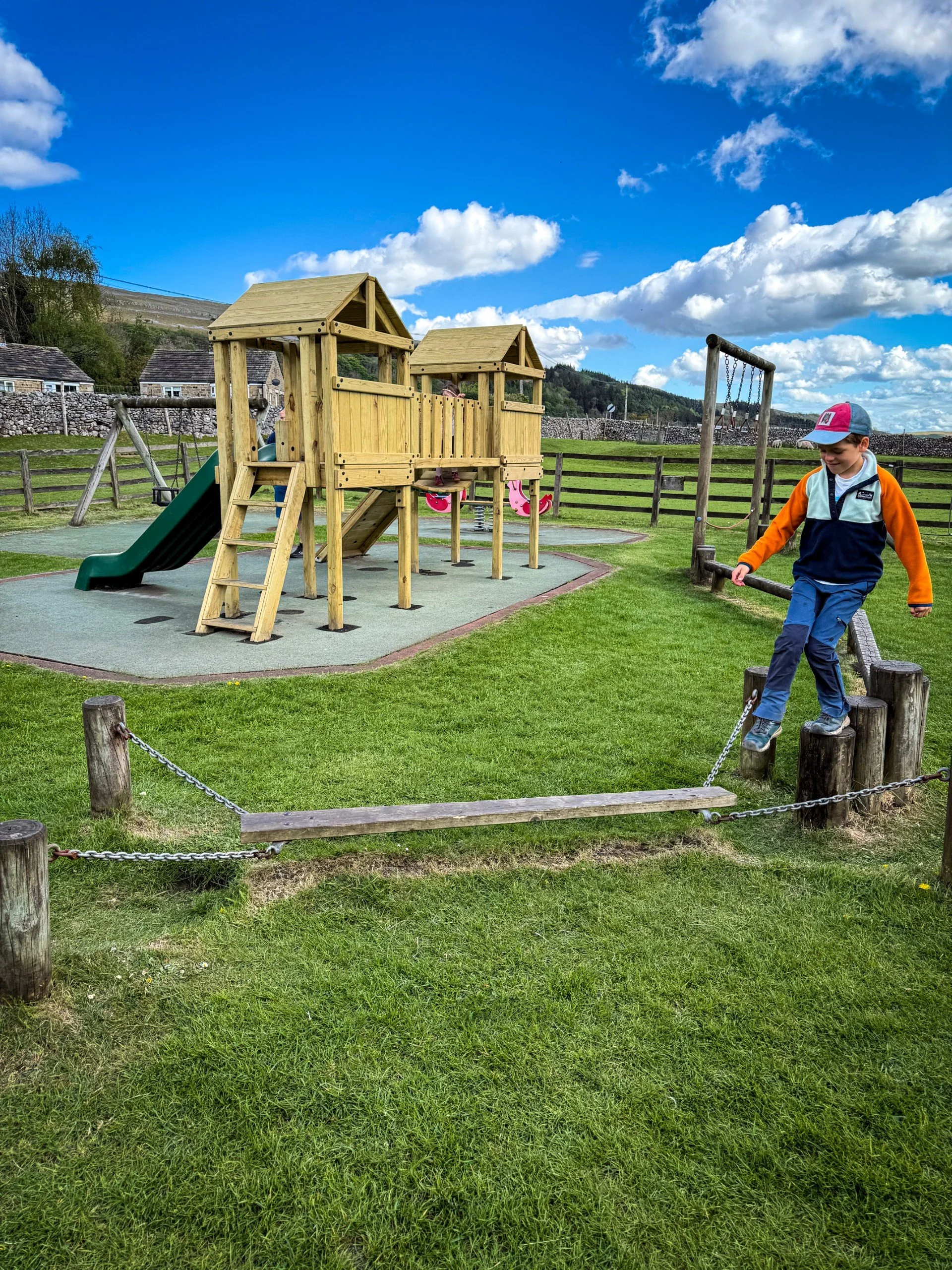 Child walking on an obstacle course with a slide and climbing frame behind at the play park