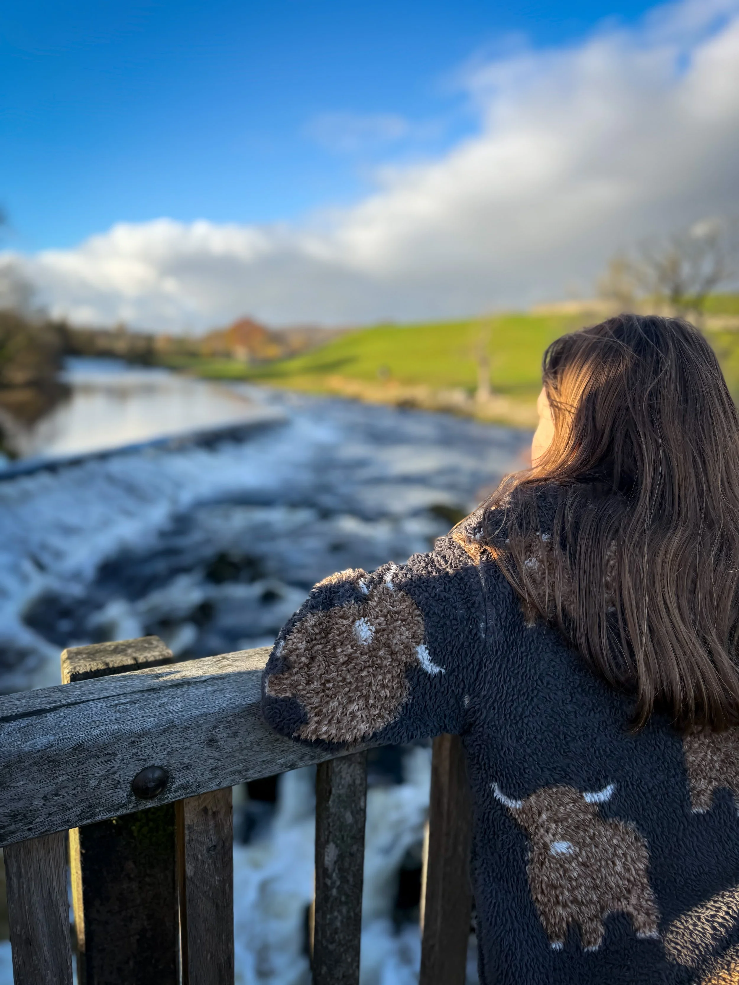 Child standing on bridge in autumn sunshine looking at a river and weir