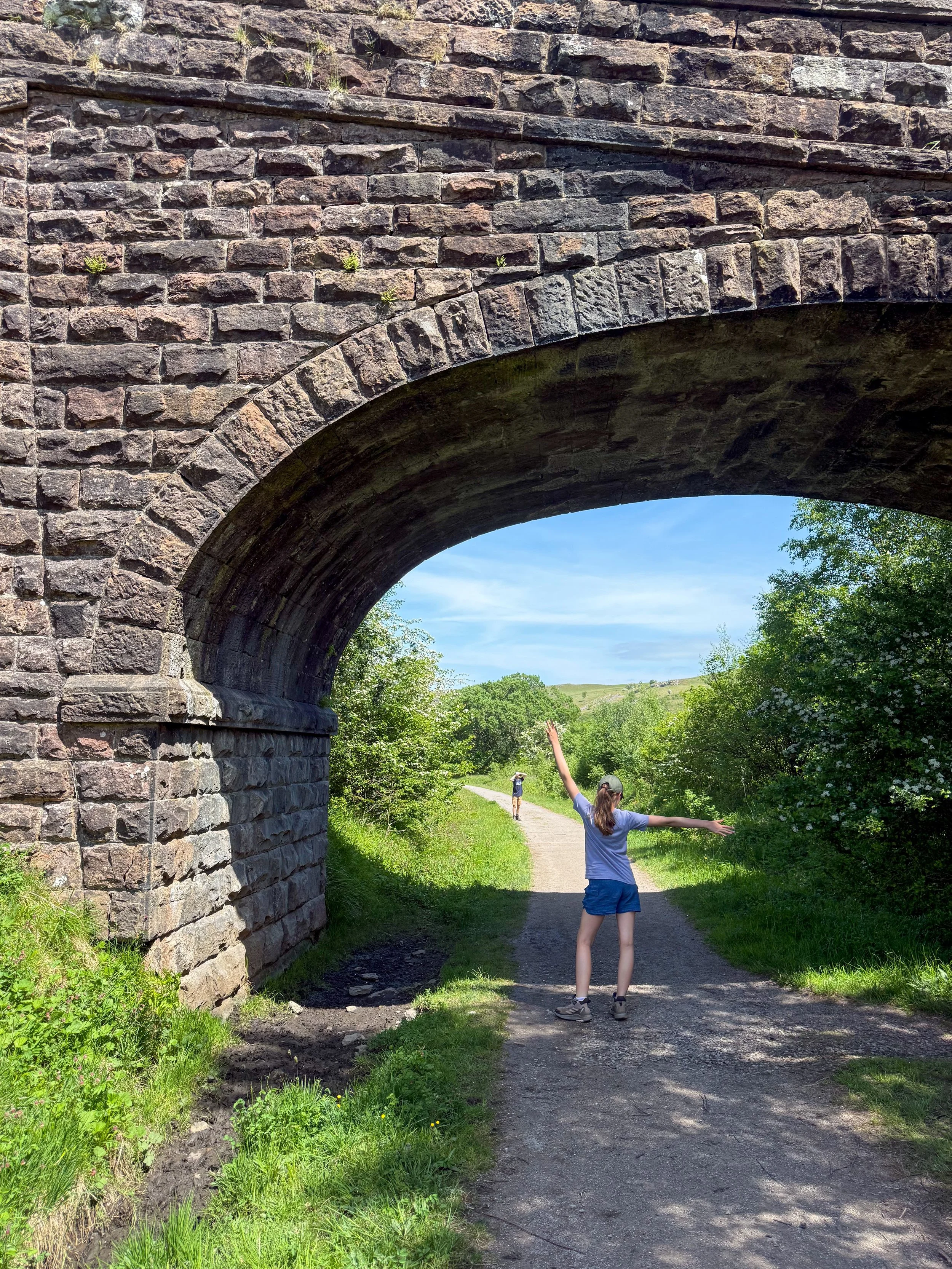 Child standing under a railway bridge with blue skies and arms in the air