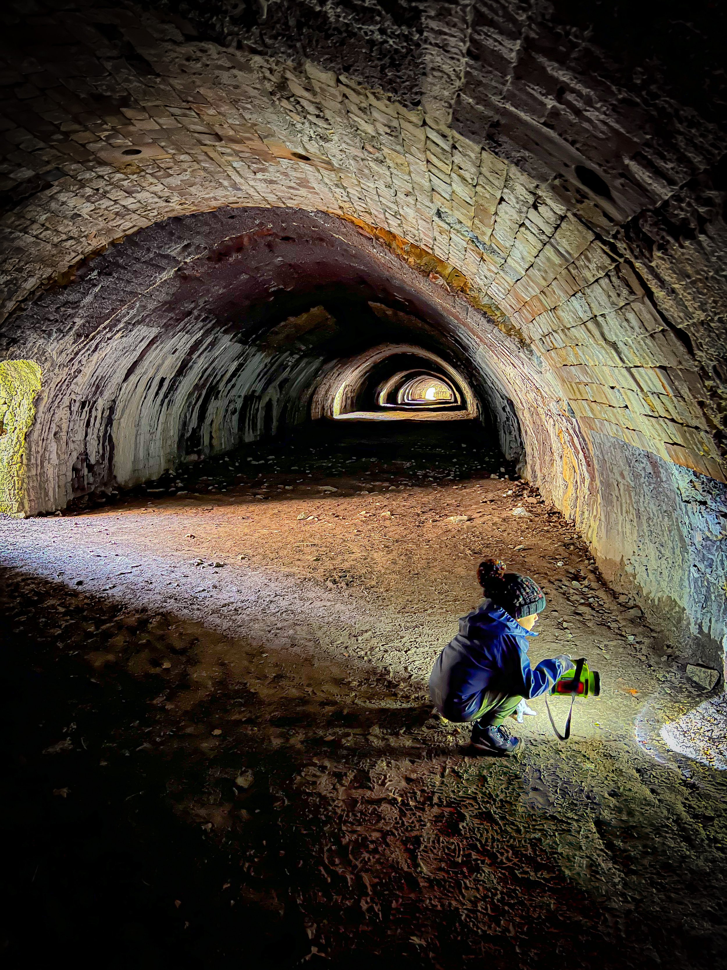 Child crouched with torch looking into a small hole inside an industrial kiln