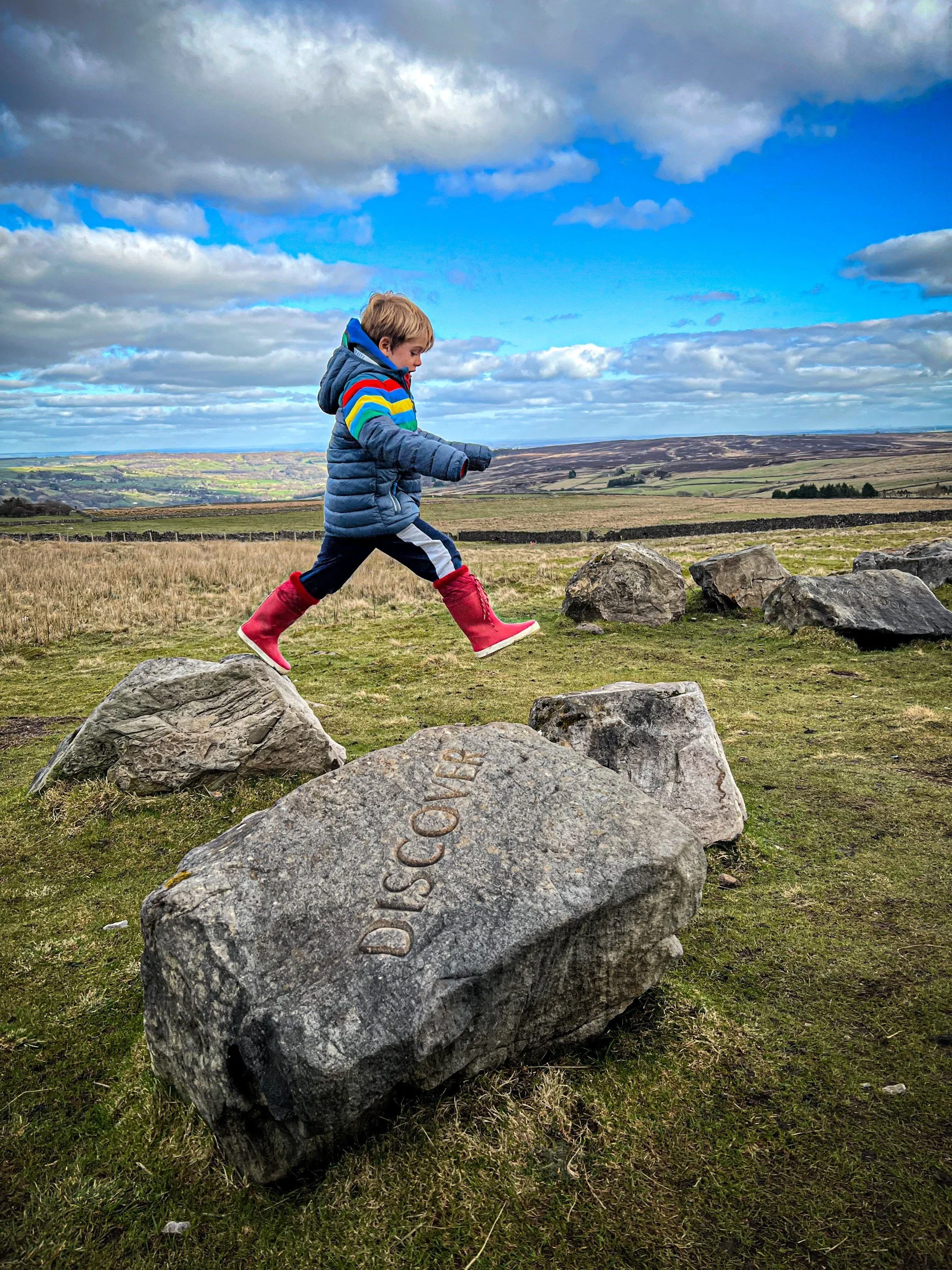 Striding from one stone to another with words in them and views of Nidderdale behind