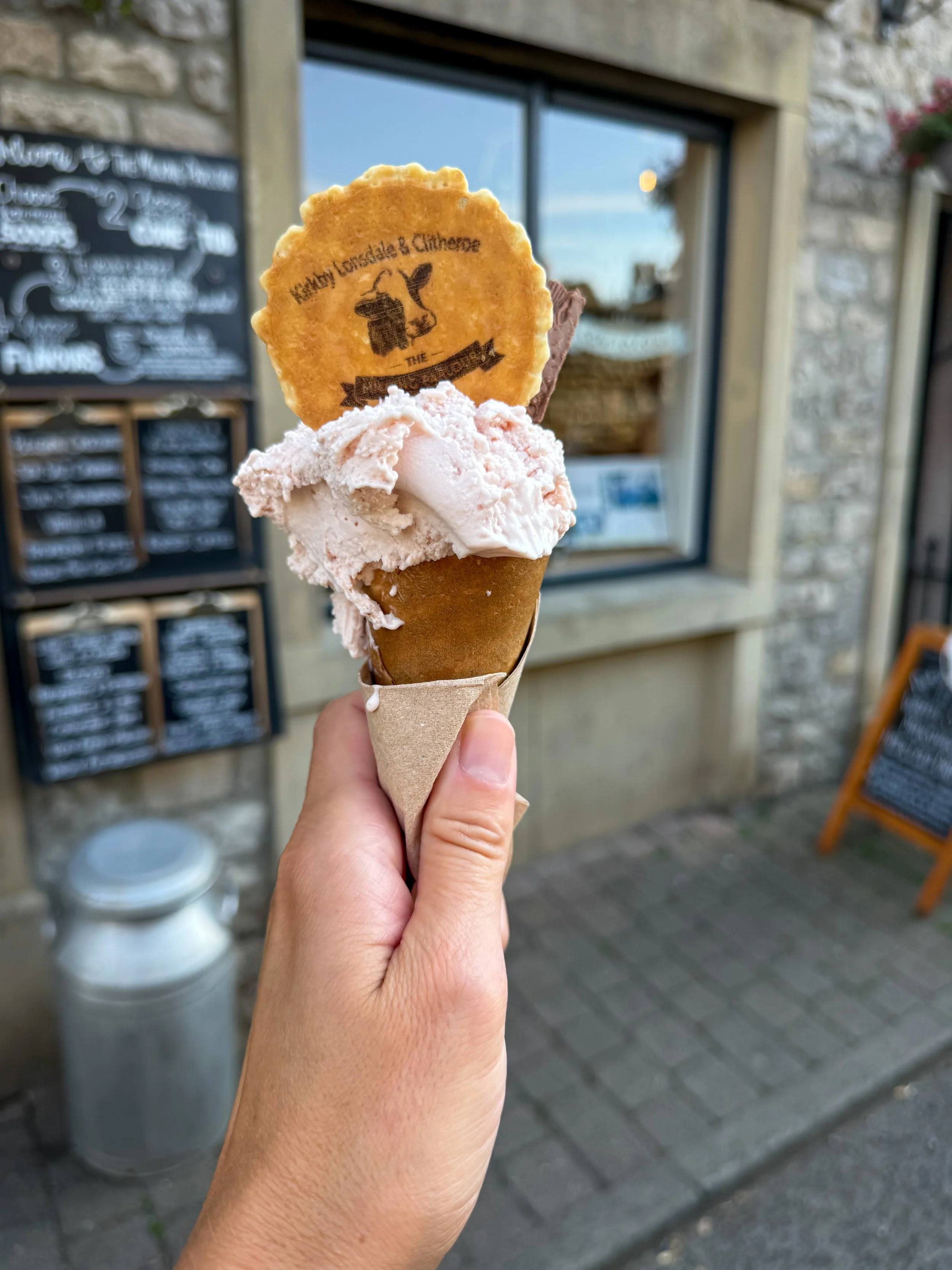 Ice cream in a hand with a wafer on the top with a cow picture on it saying kirkby lonsdale and clitheroe