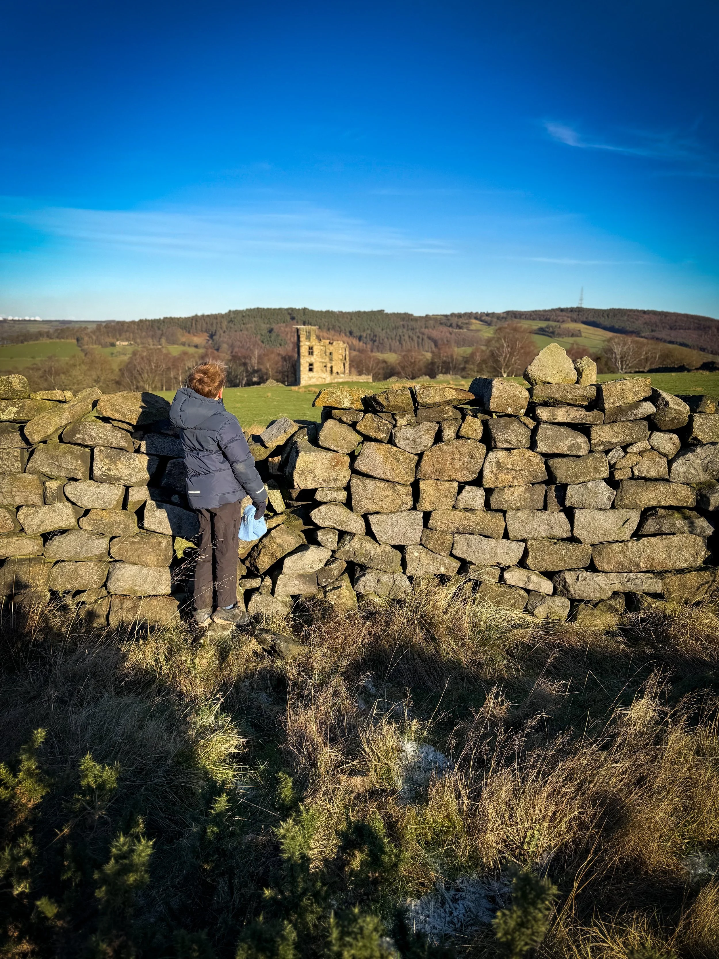 Child standing at dry stone wall with ruins behind and blue sky