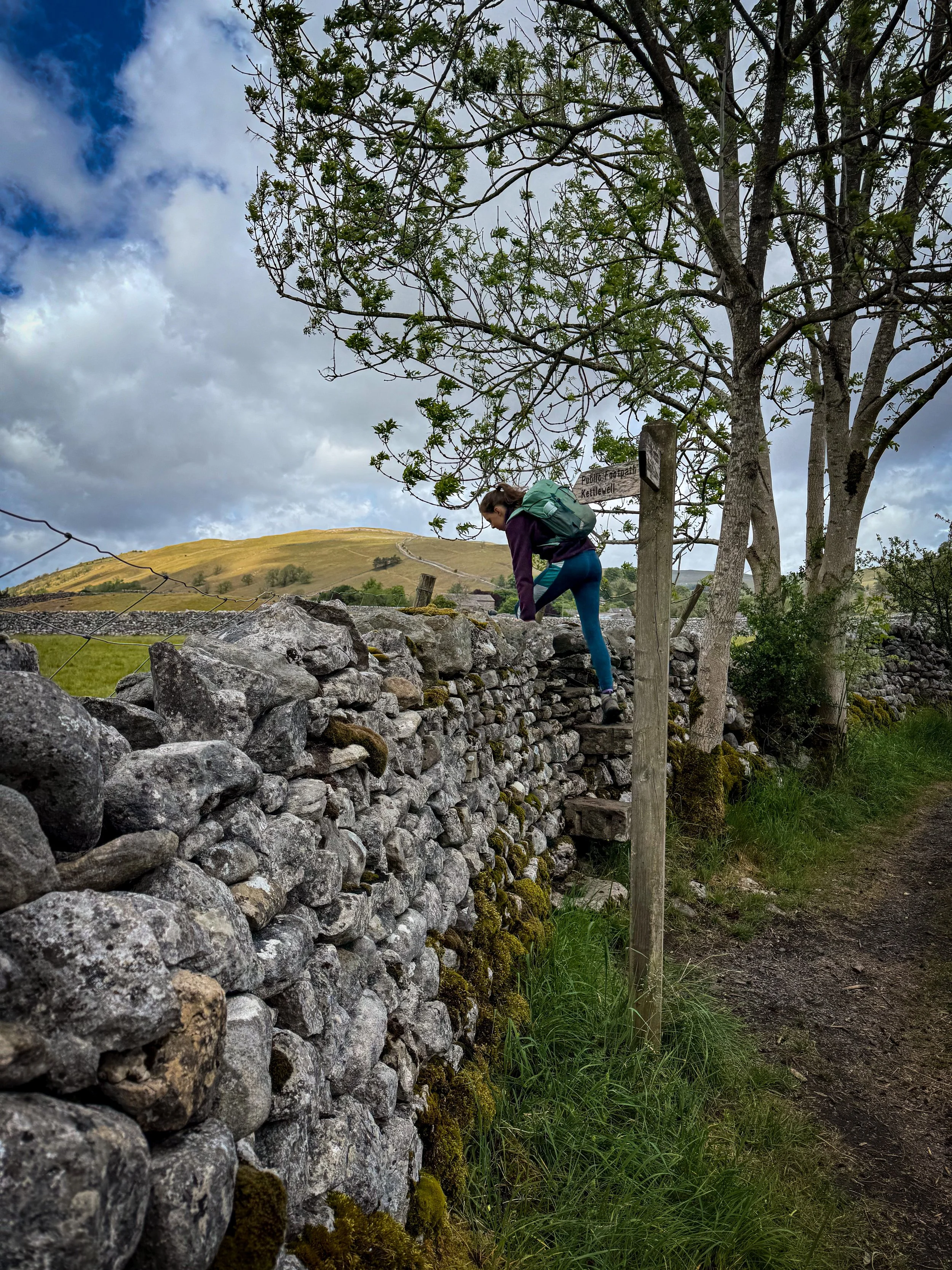 Child climbing dry stone wall on a stile with a signpost